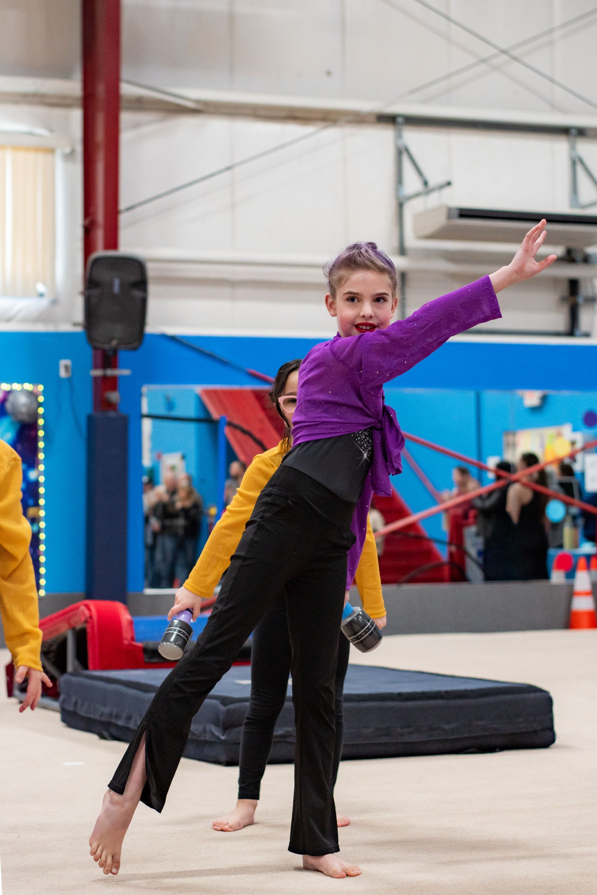 Young gymnast in purple and black balancing on one leg in a gym studio