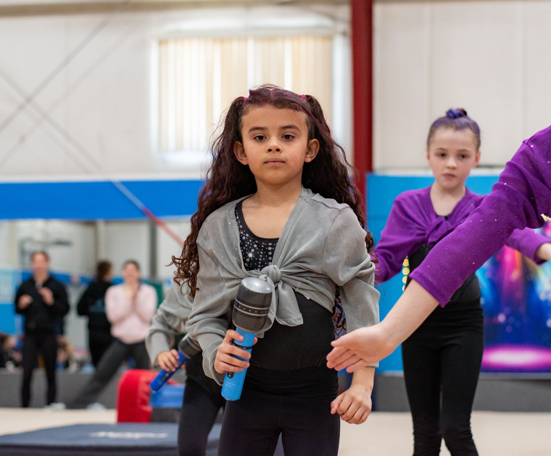 Children on a gym floor holding microphones during a dance or performance rehearsal
