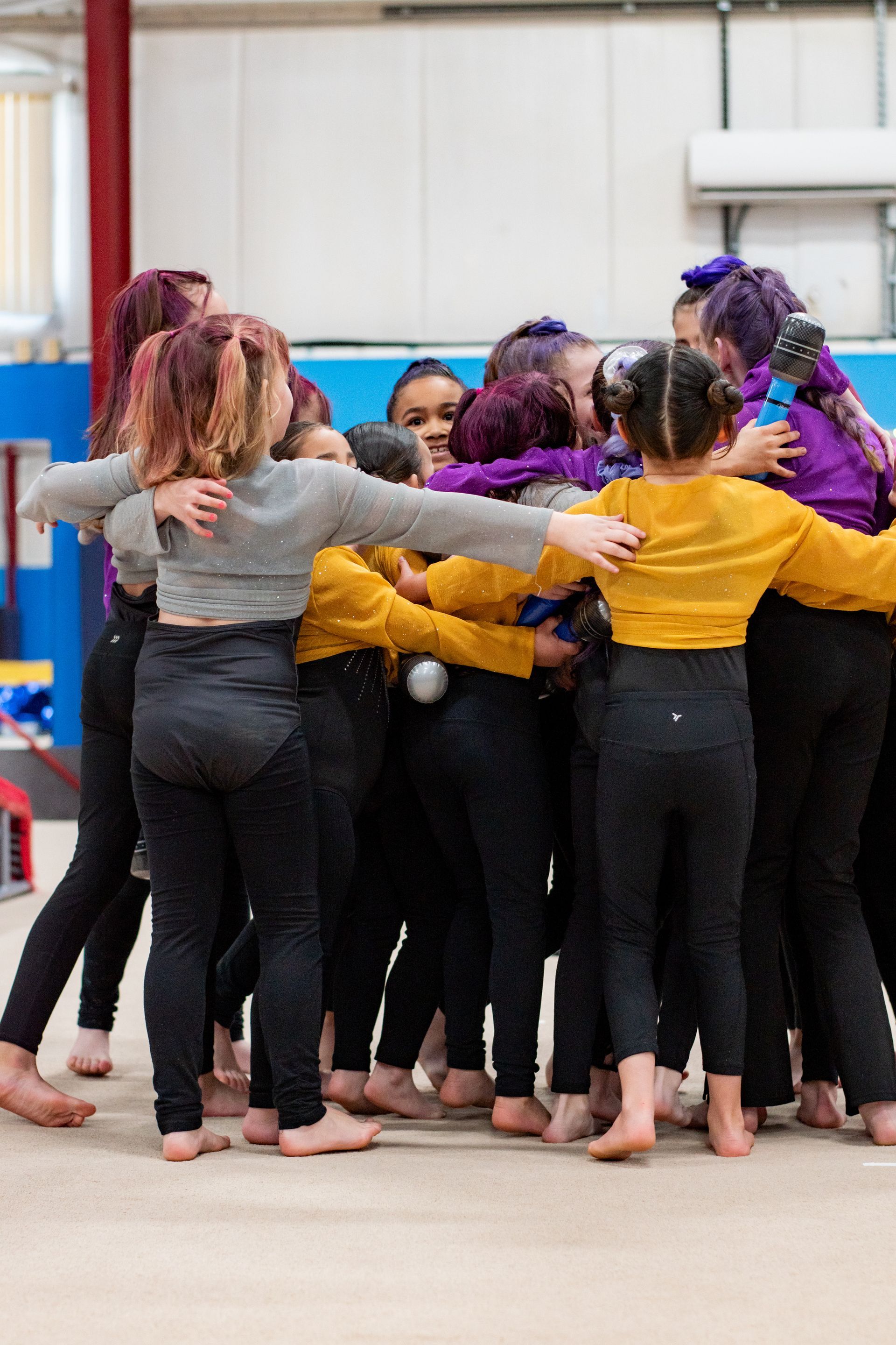 Group of dancers in colorful tops huddle together in a studio, arms around each other.
