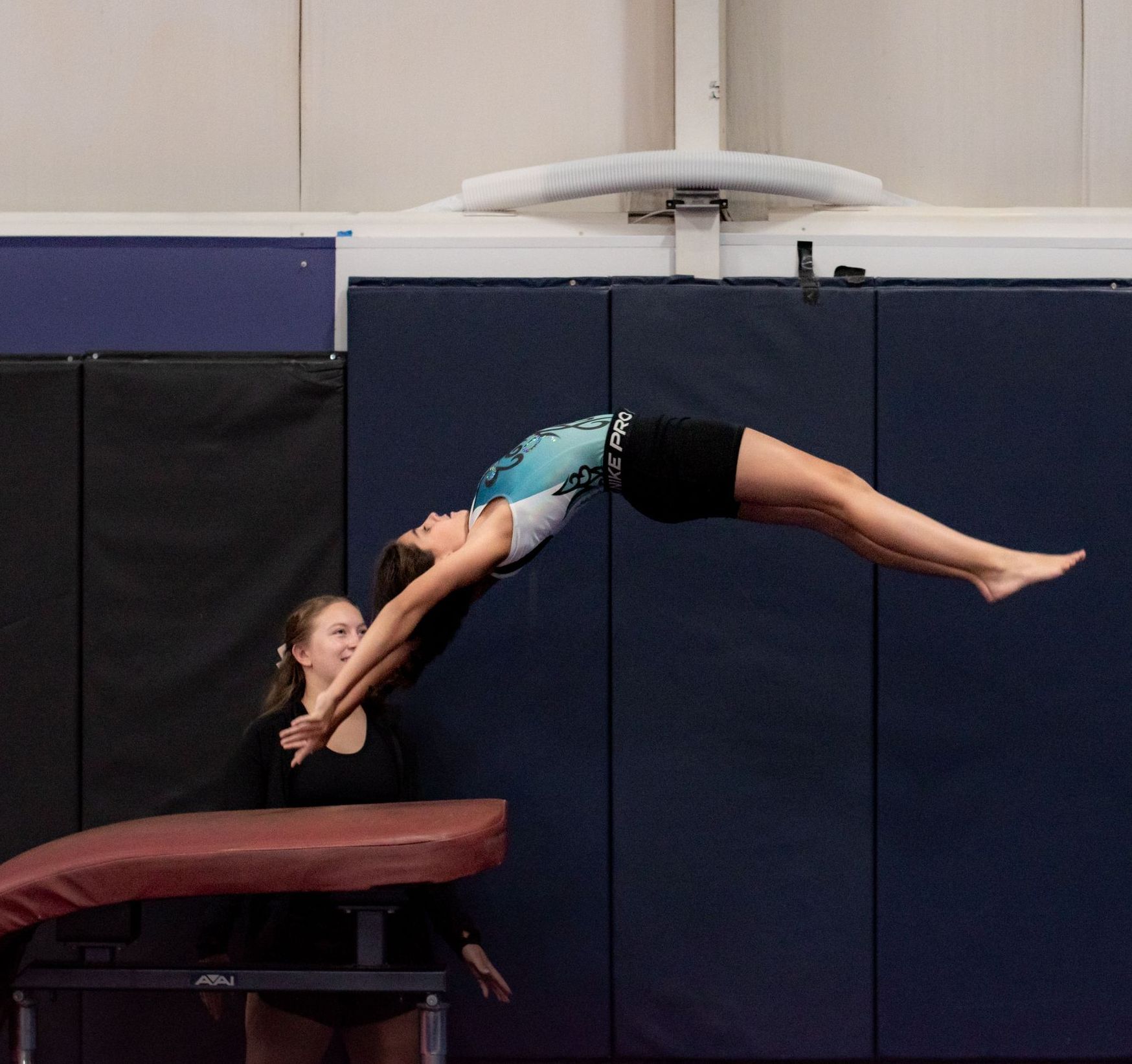 Gymnast arching over a coach’s hands onto a padded mat in a gym
