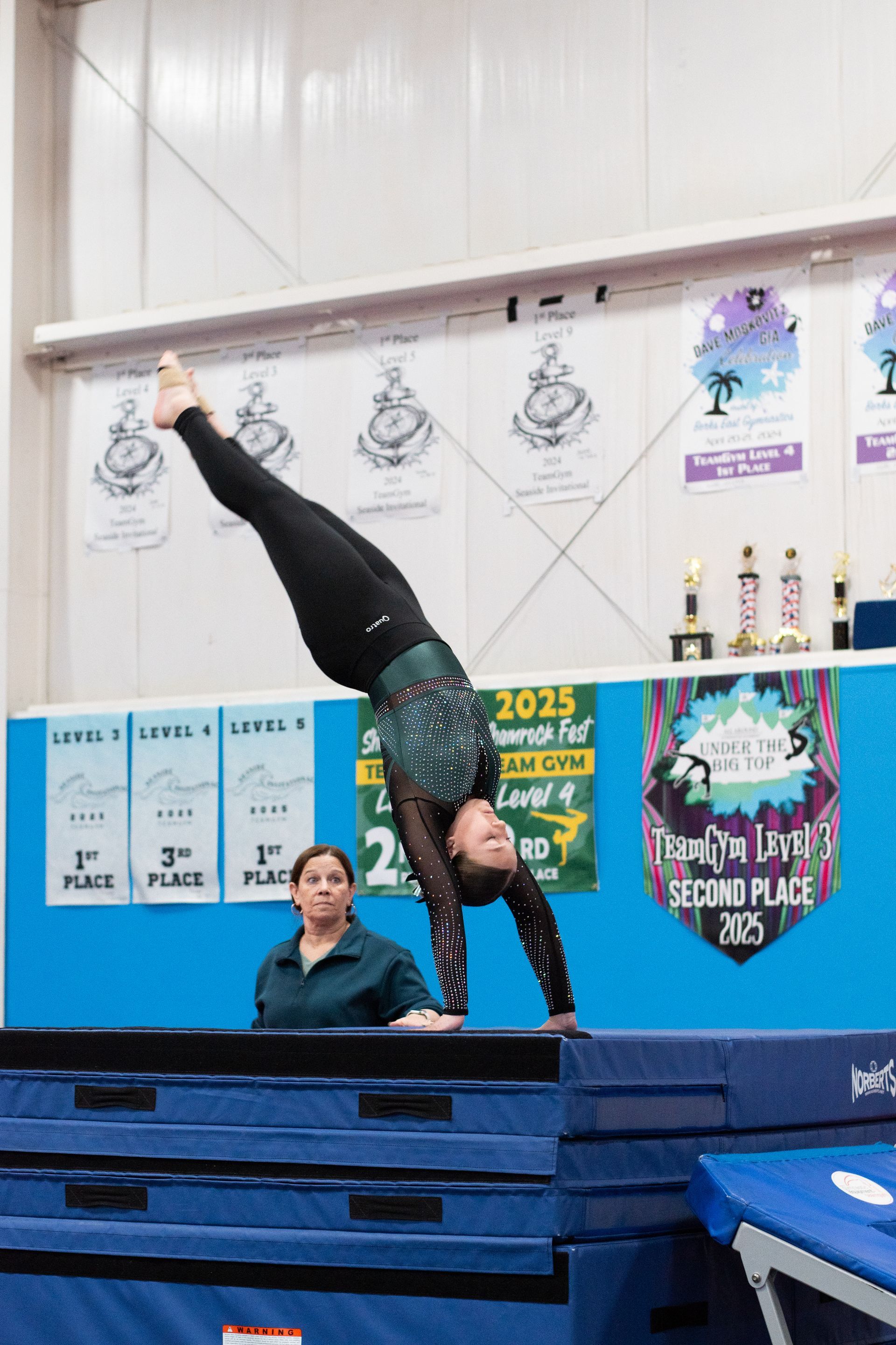 Gymnast balancing upside down on one hand on a blue mat in an indoor competition venue