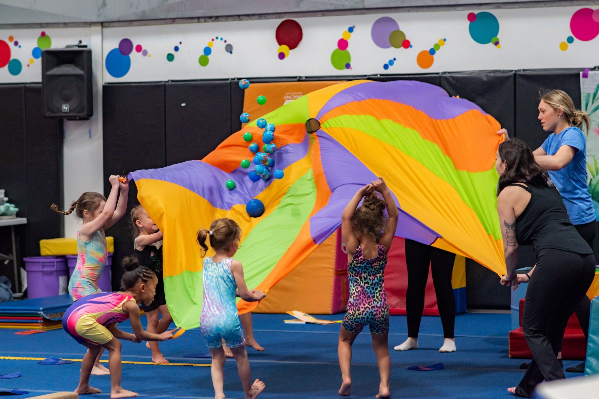 Children playing with a colorful parachute in a gym decorated with balloons