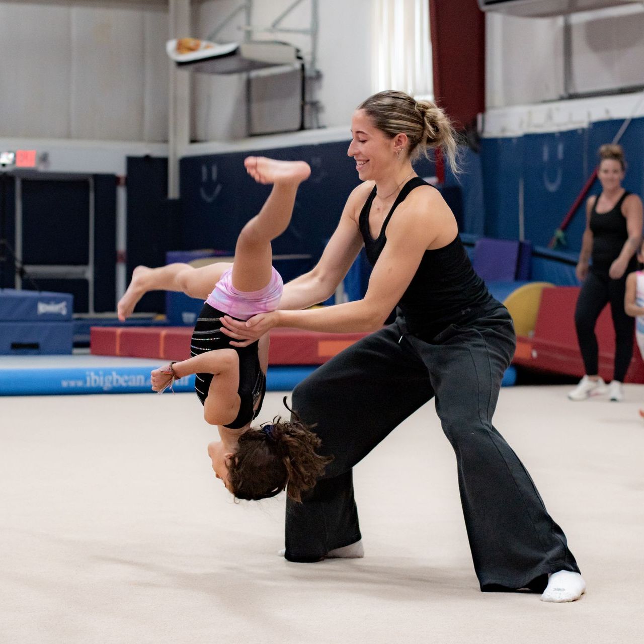 Gymnastics coach spotting a child doing a handstand flip in a gymnasium
