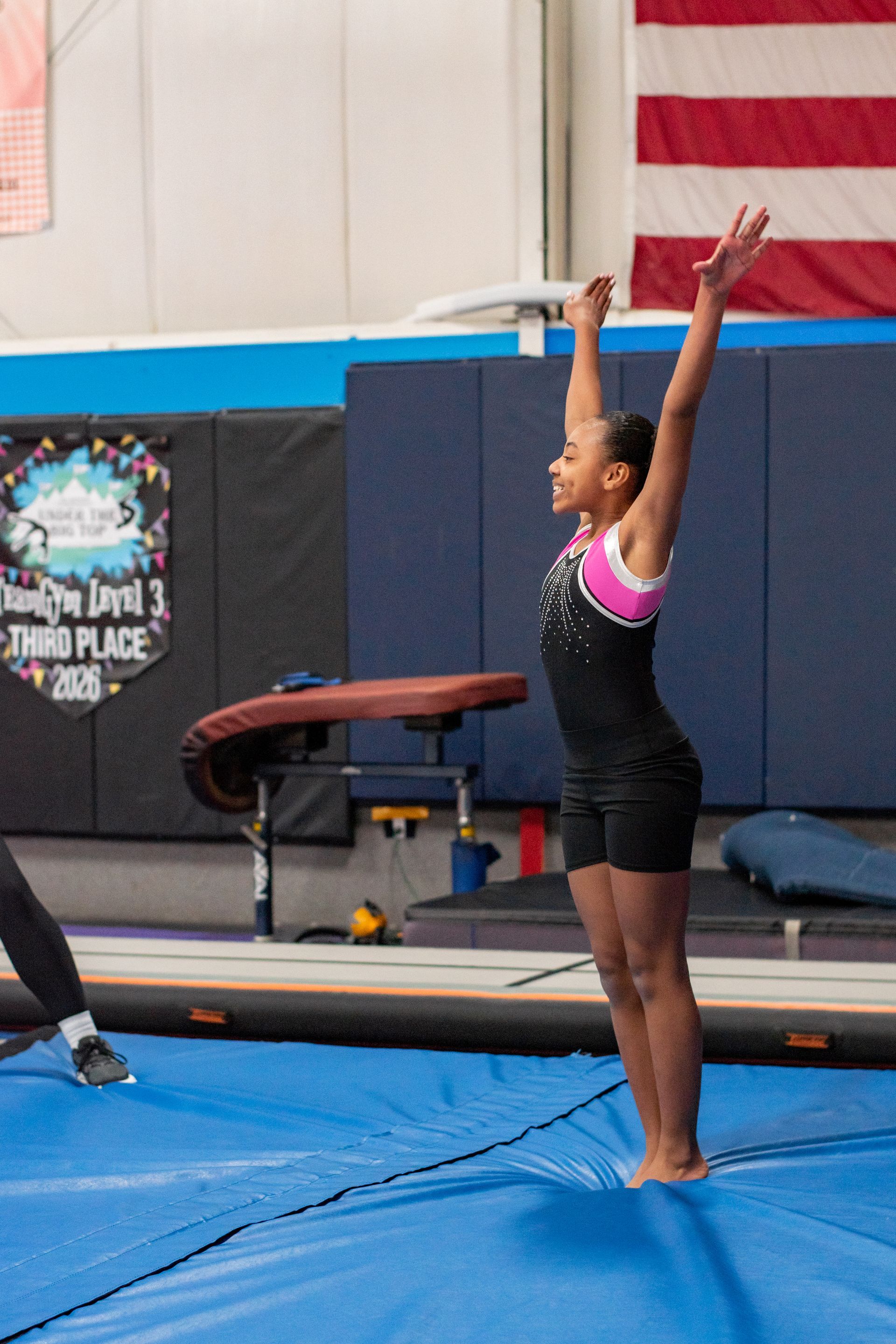 Gymnast standing with arms raised on a blue mat in an indoor gym