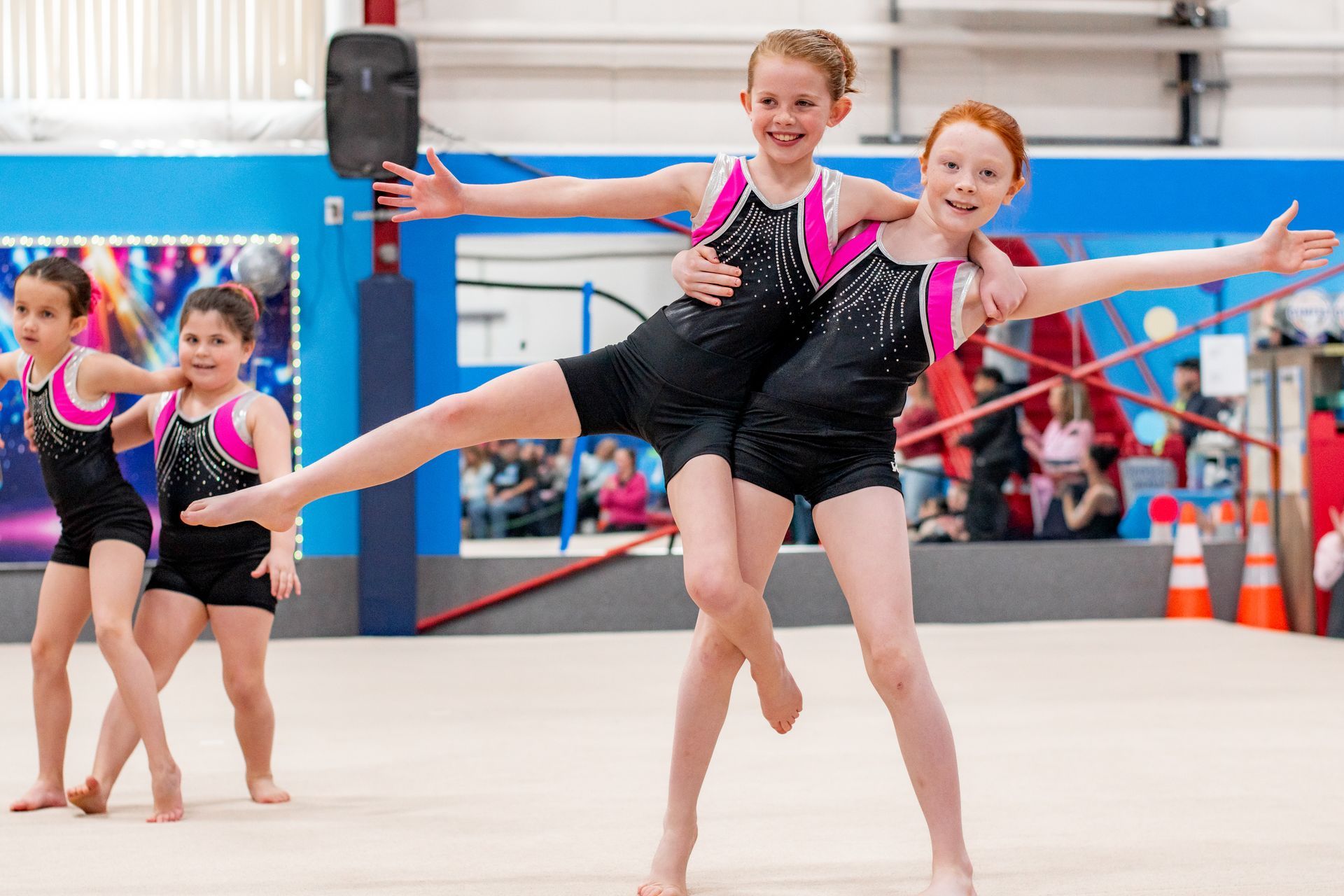 Two gymnasts in black leotards posing on a floor mat during a gymnastics routine