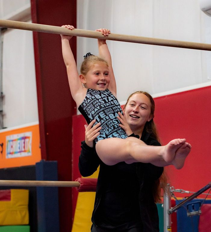 Adult holding a smiling child on gymnastics bars in a colorful gym
