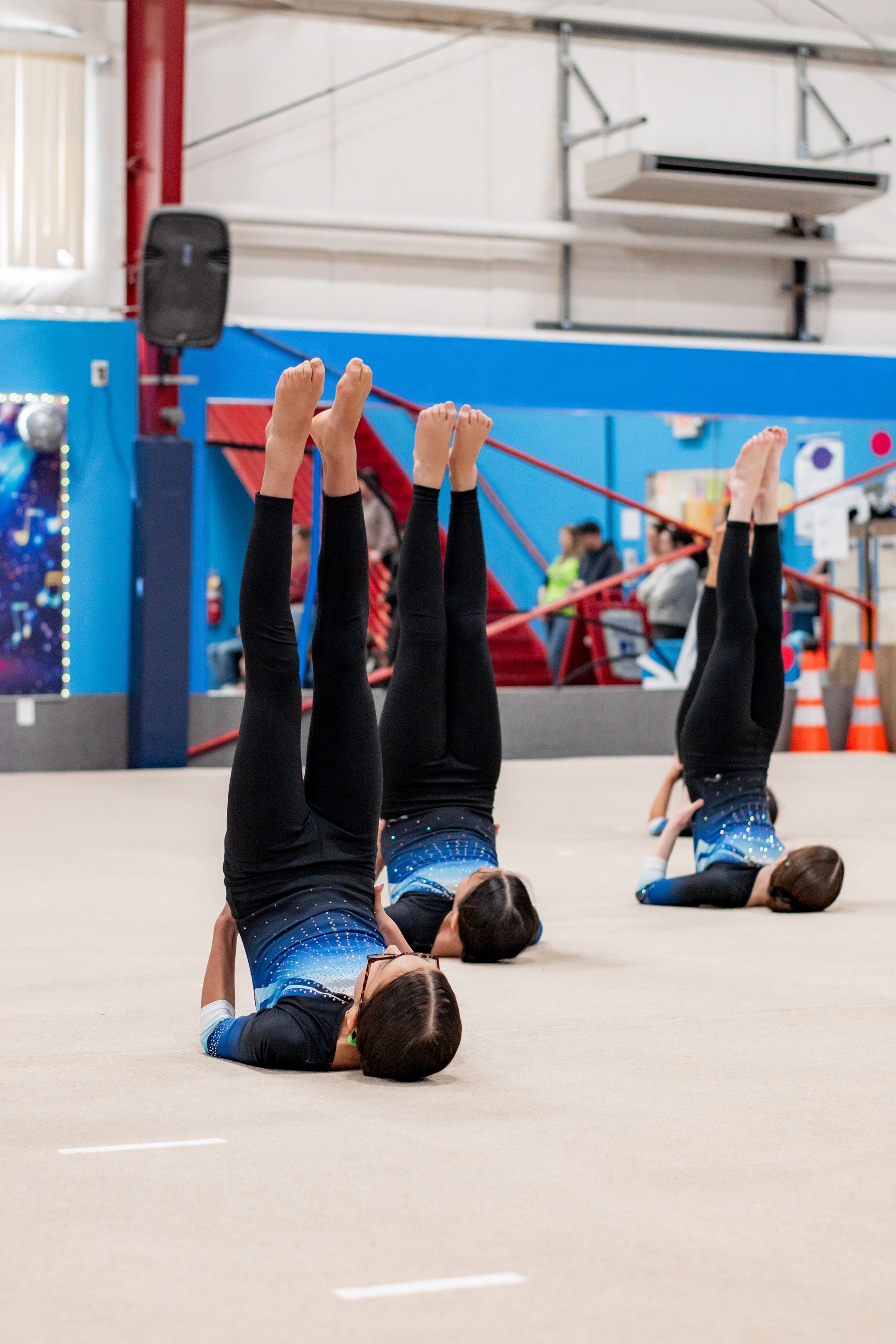 Gymnasts practicing shoulder stands on a mat in an indoor gym.