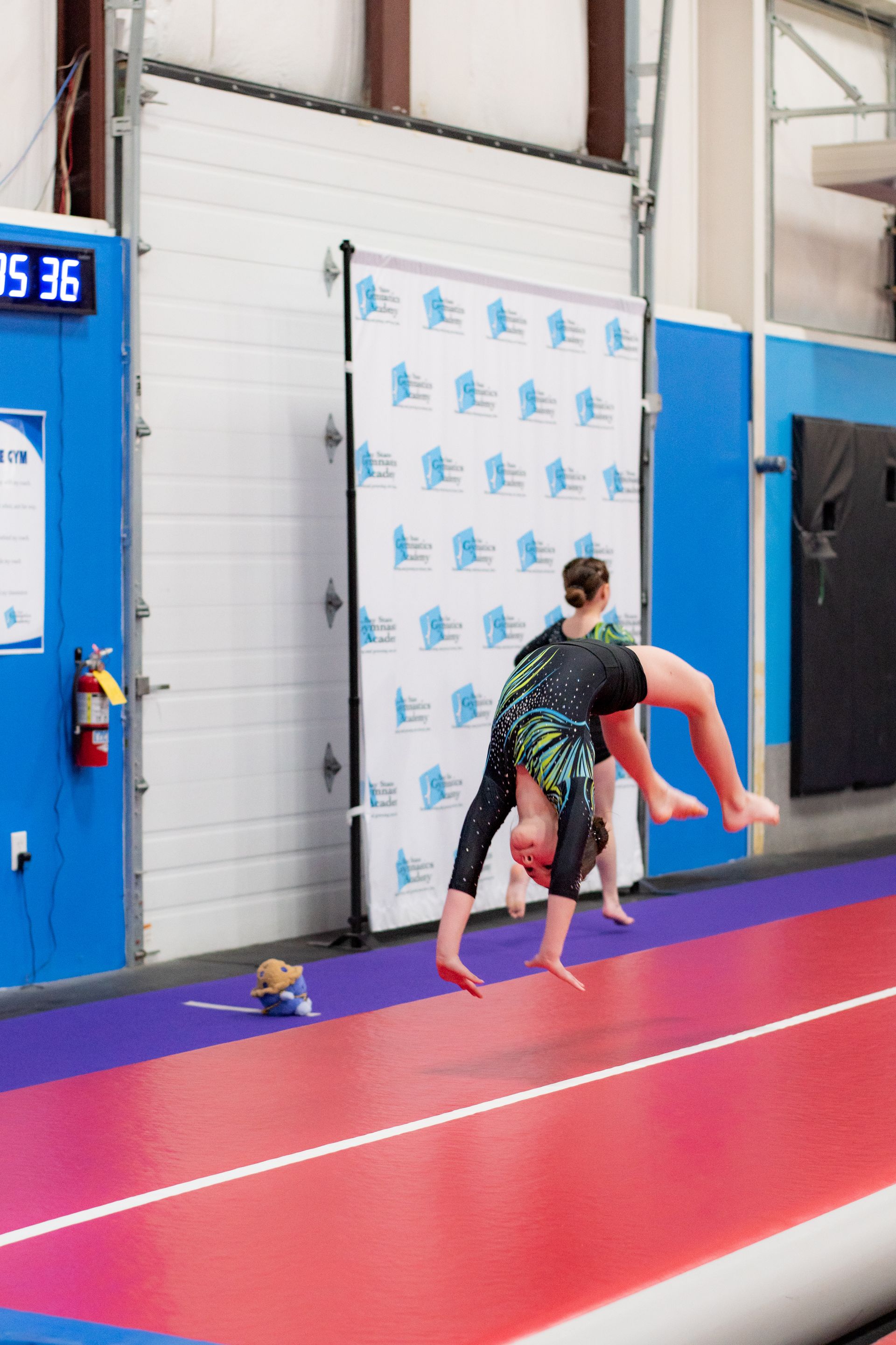 Person carrying another person in a gym on a red mat near a blue wall