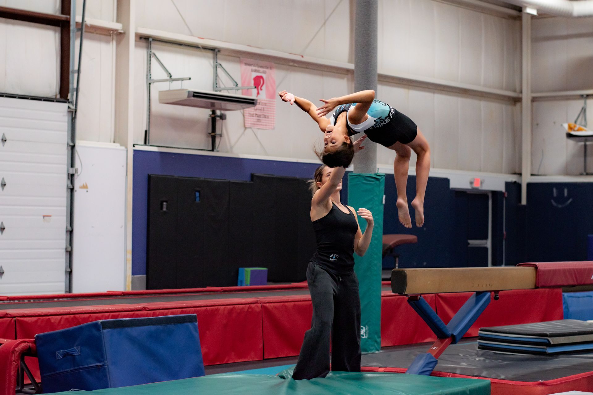 Gymnasts performing an overhead balance lift on a mat in an indoor gym