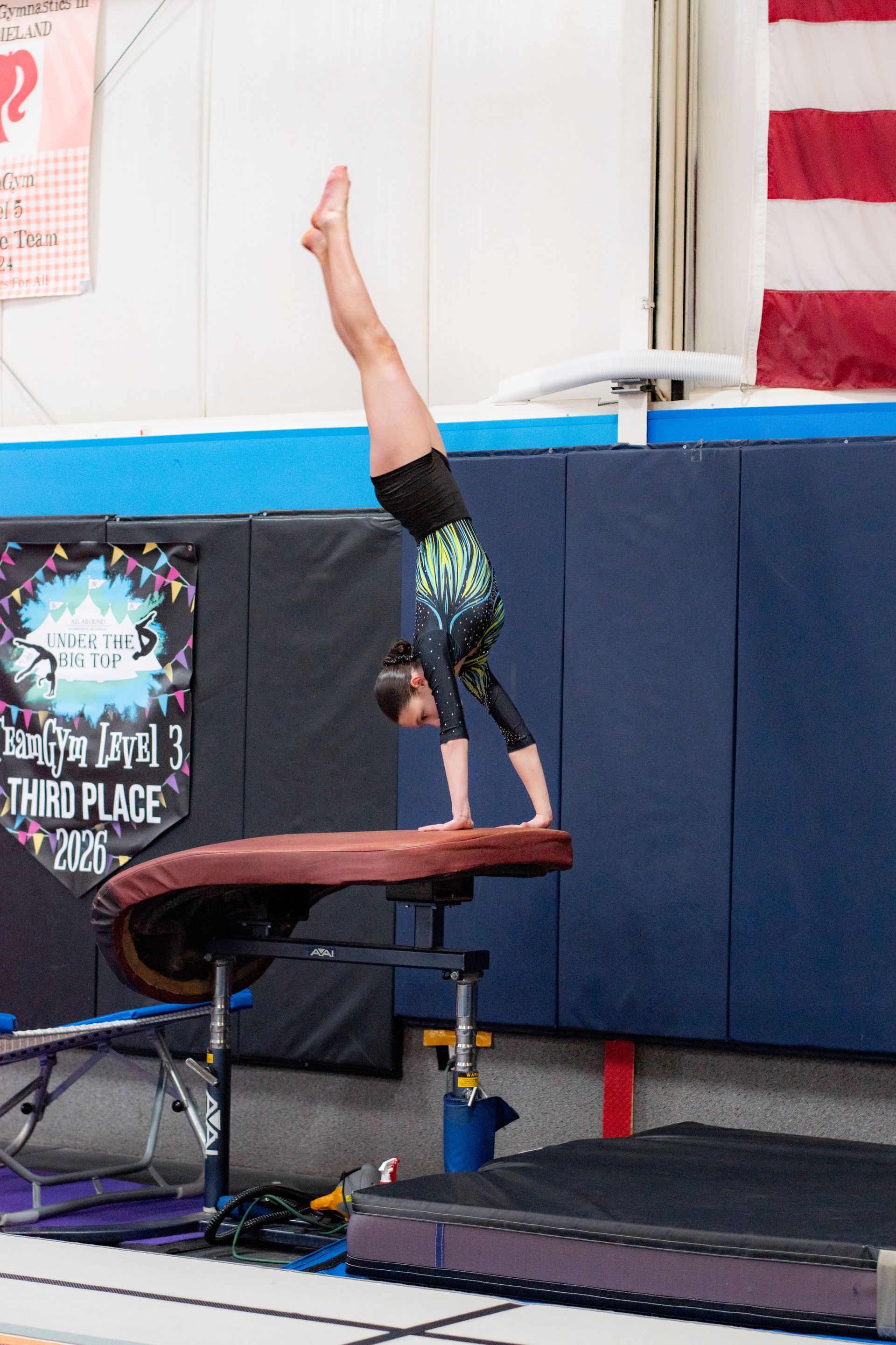 Gymnast doing a handstand on a balance beam in an indoor gym.