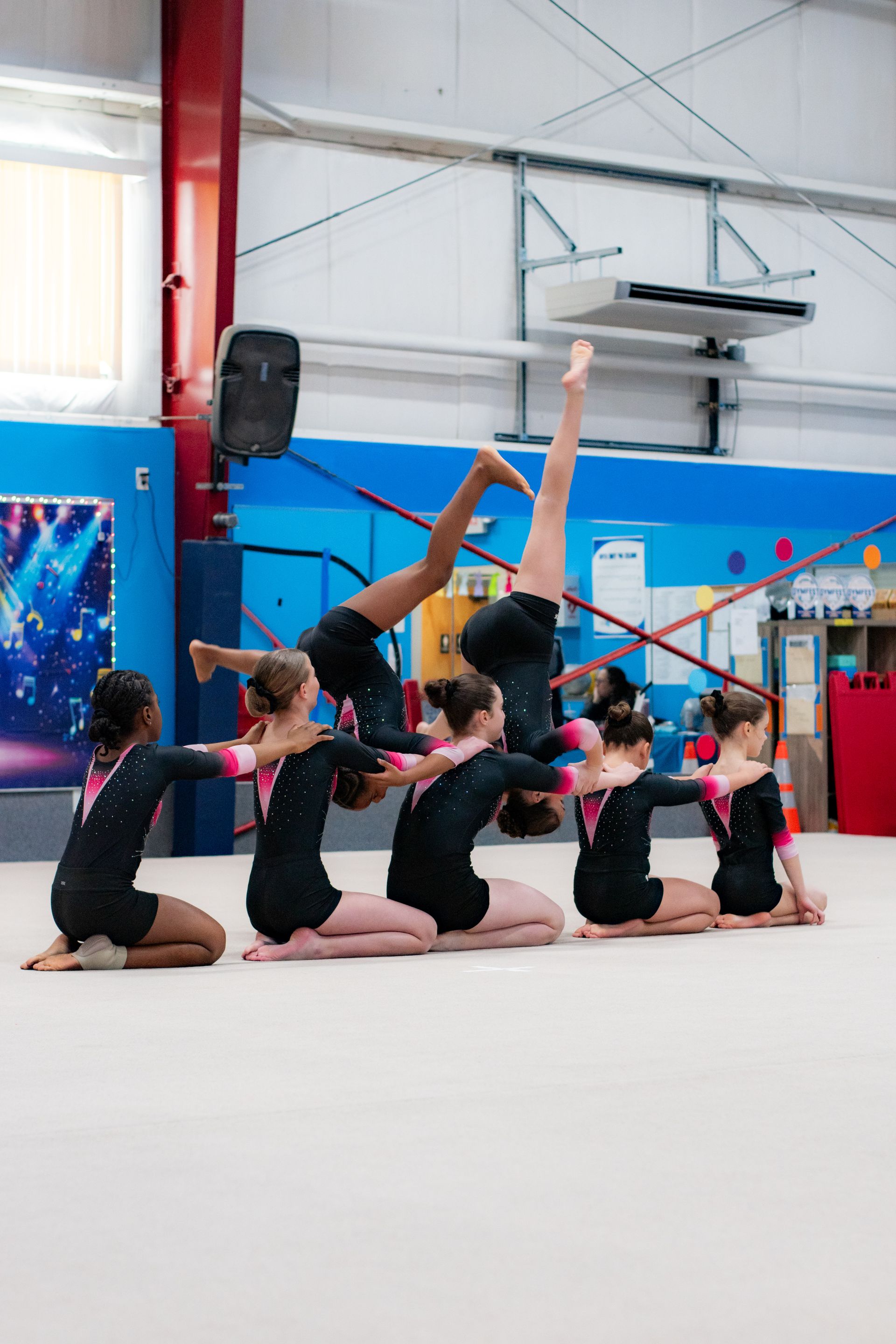 Gymnasts in black leotards pose in a floor routine inside a bright indoor gym