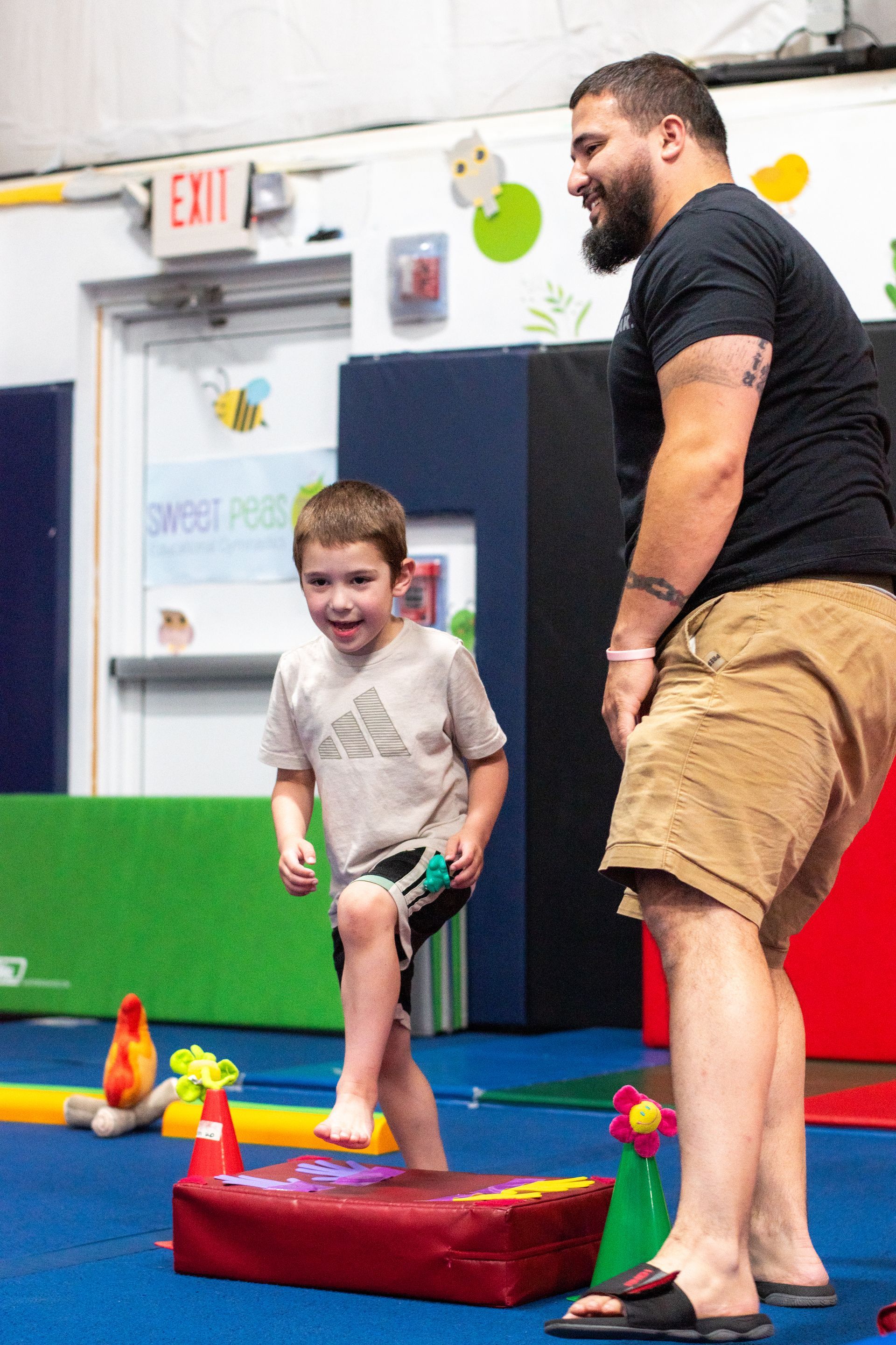 Two people standing on foam blocks in a colorful gym, smiling during an activity