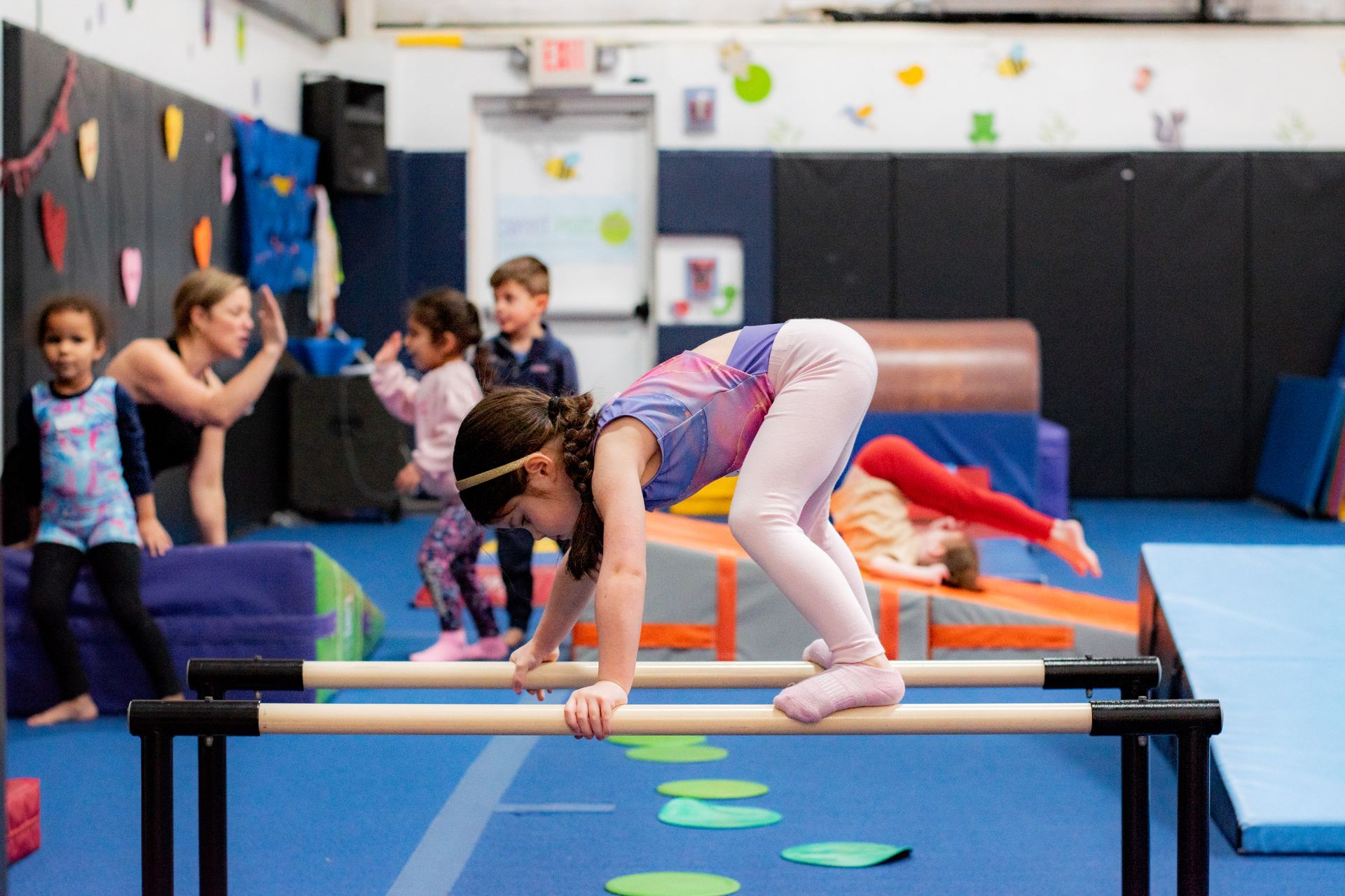Child balancing on parallel bars in a gym class while other children watch and exercise nearby