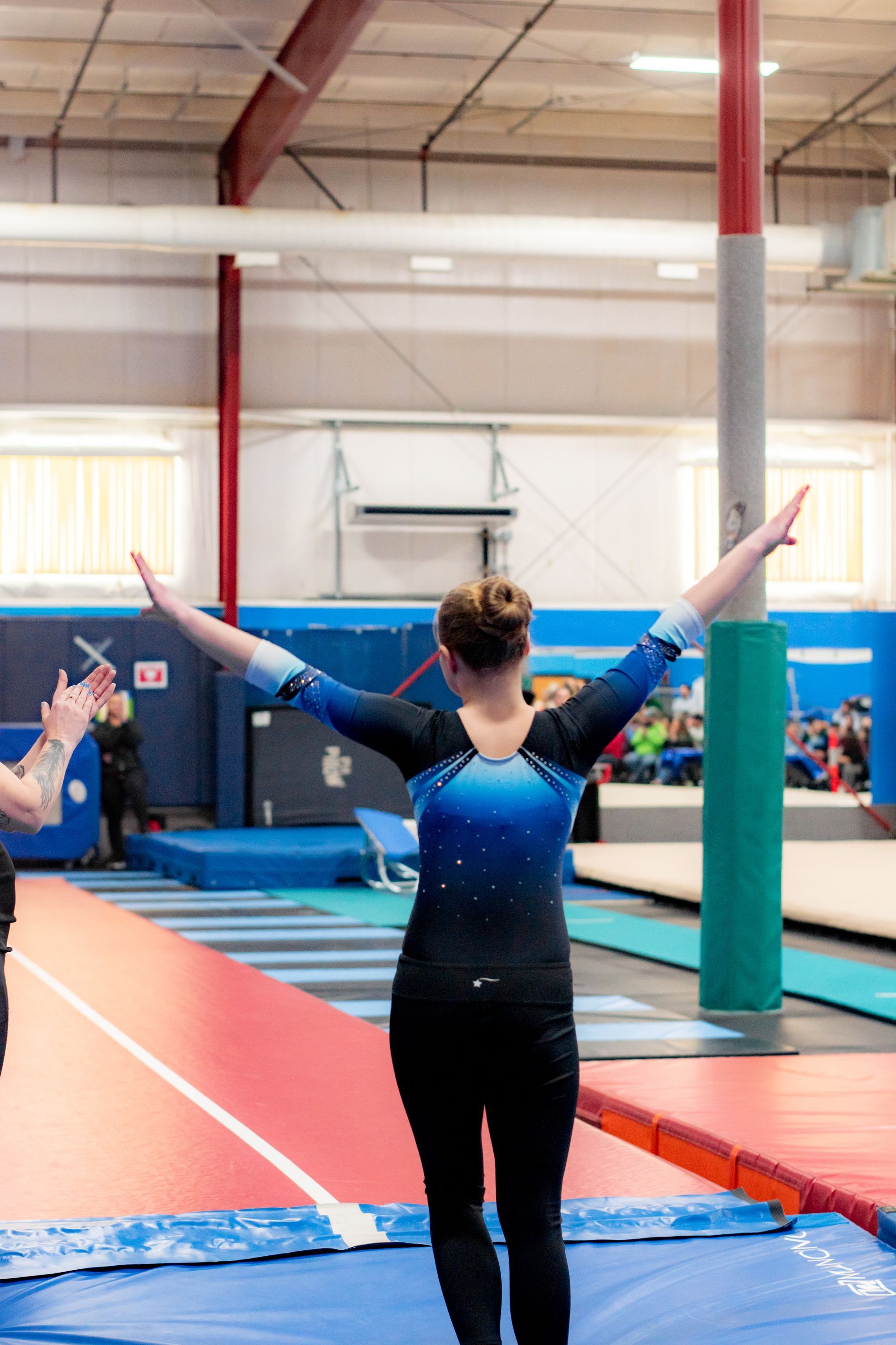 Gymnast on a floor mat with arms raised in a gymnasium
