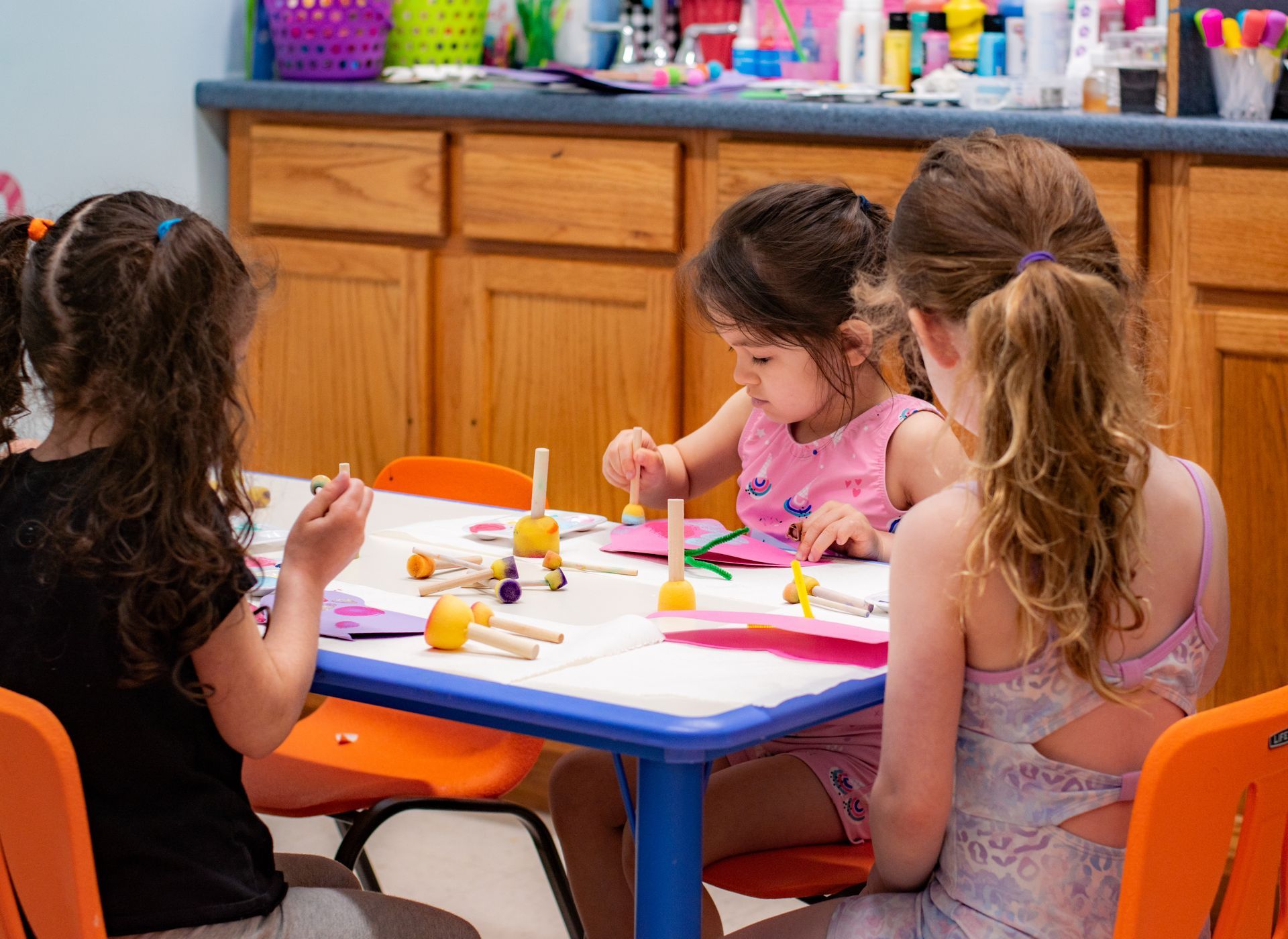 Children coloring at a table in a classroom, with crayons and paper on an orange-and-blue table
