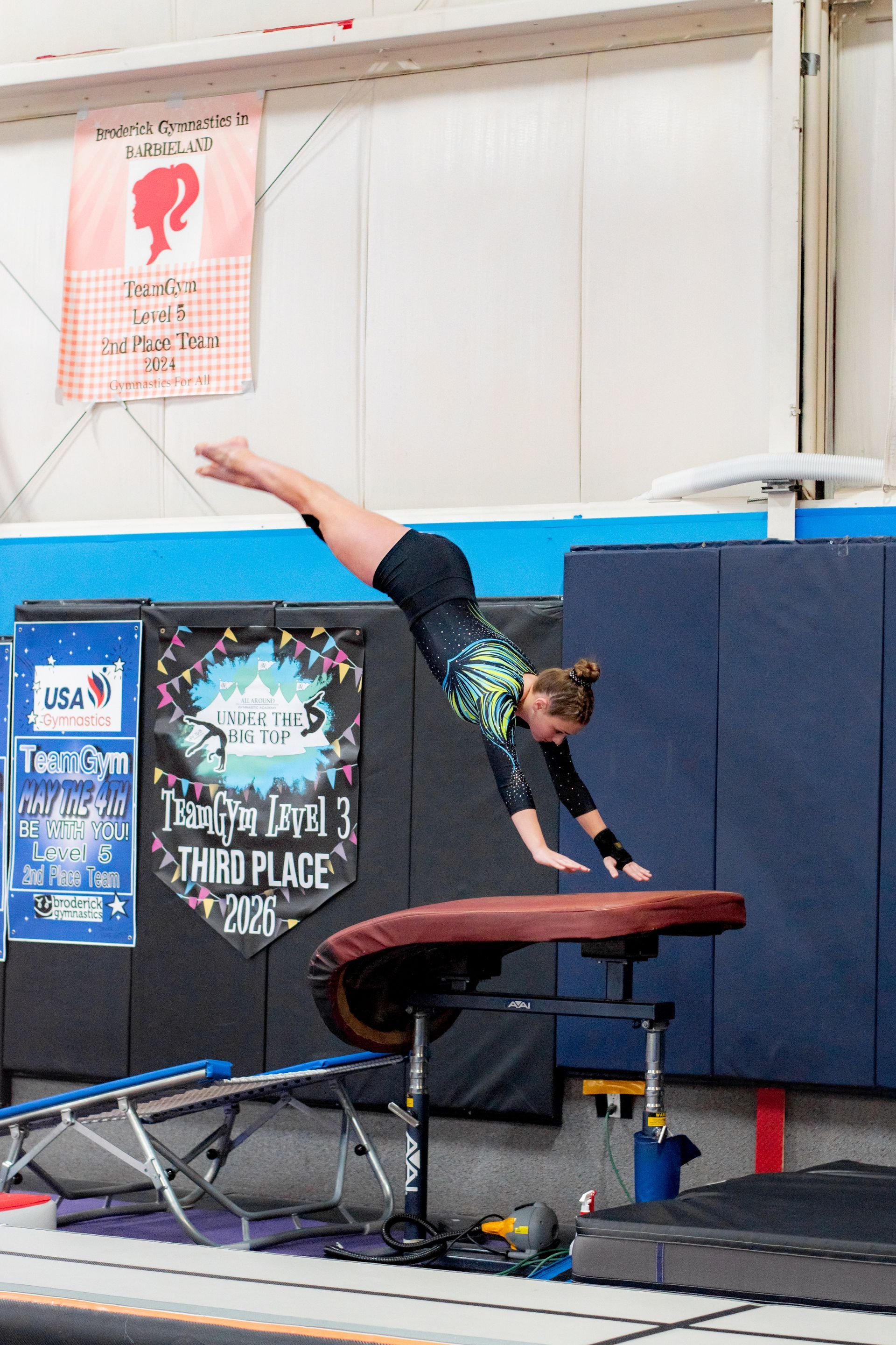 Gymnast performing a handstand on a balance beam in an indoor gym.