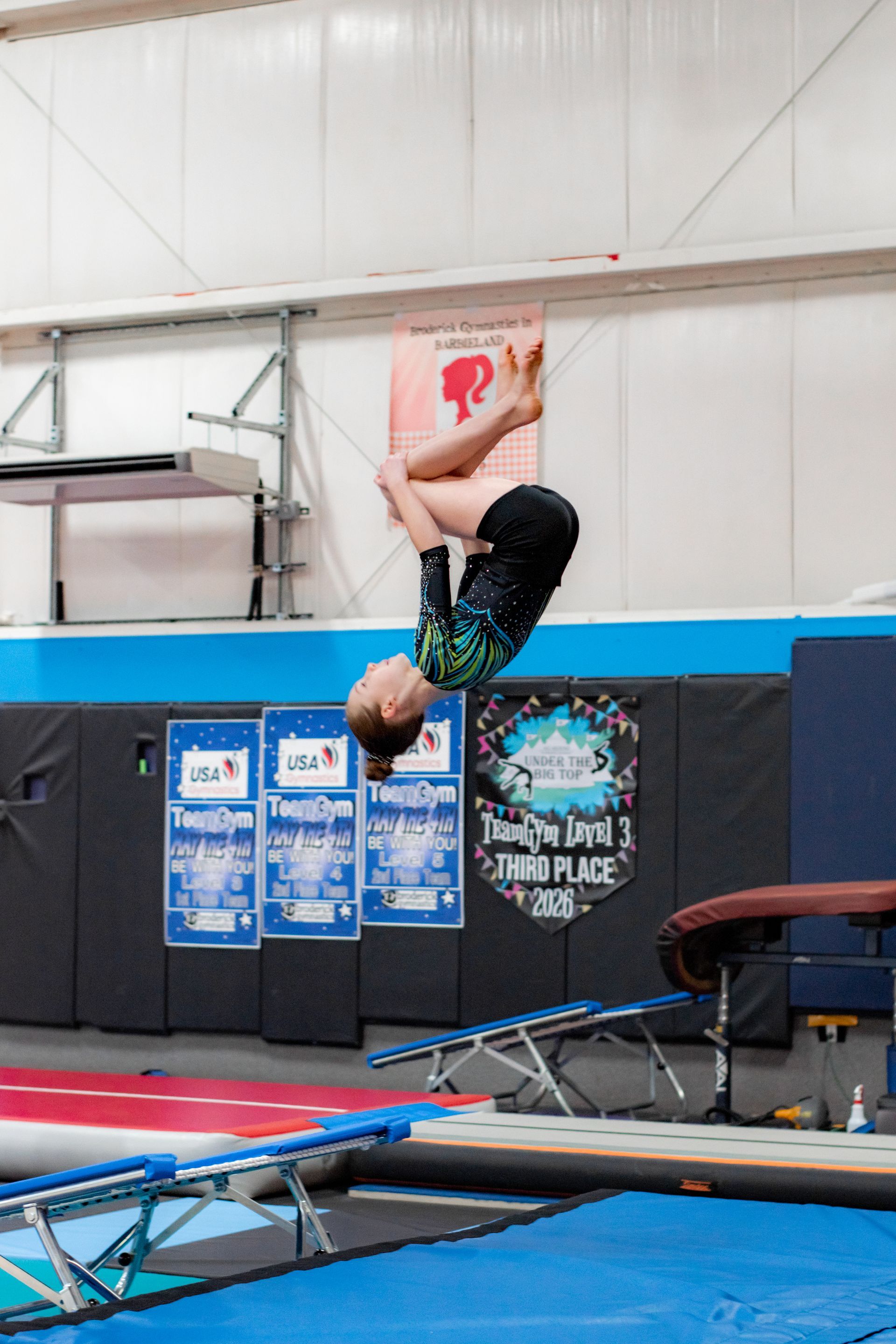 Gymnast mid-backflip above a trampoline in an indoor training facility