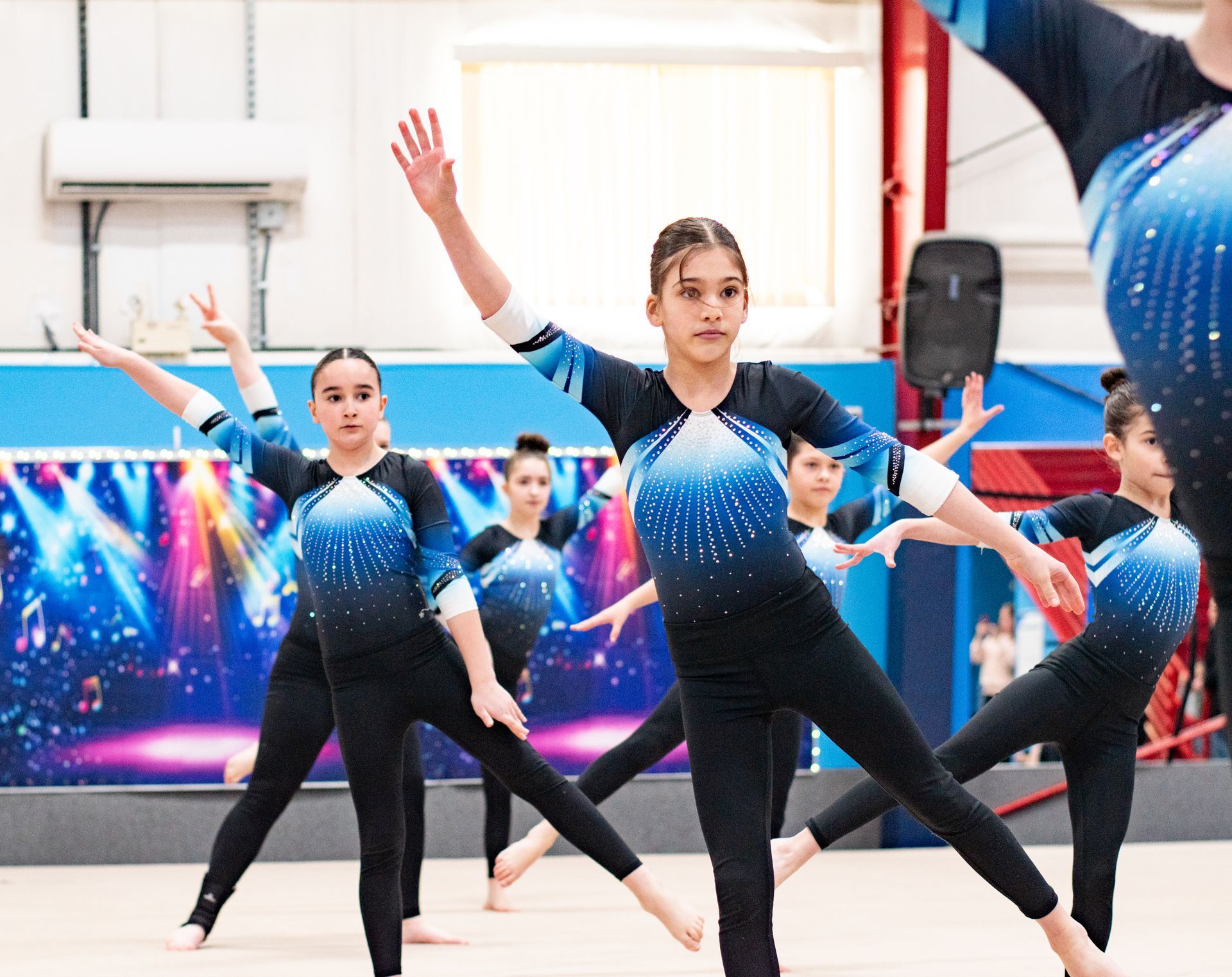 Gymnasts in blue-and-black leotards posing in a bright indoor training gym
