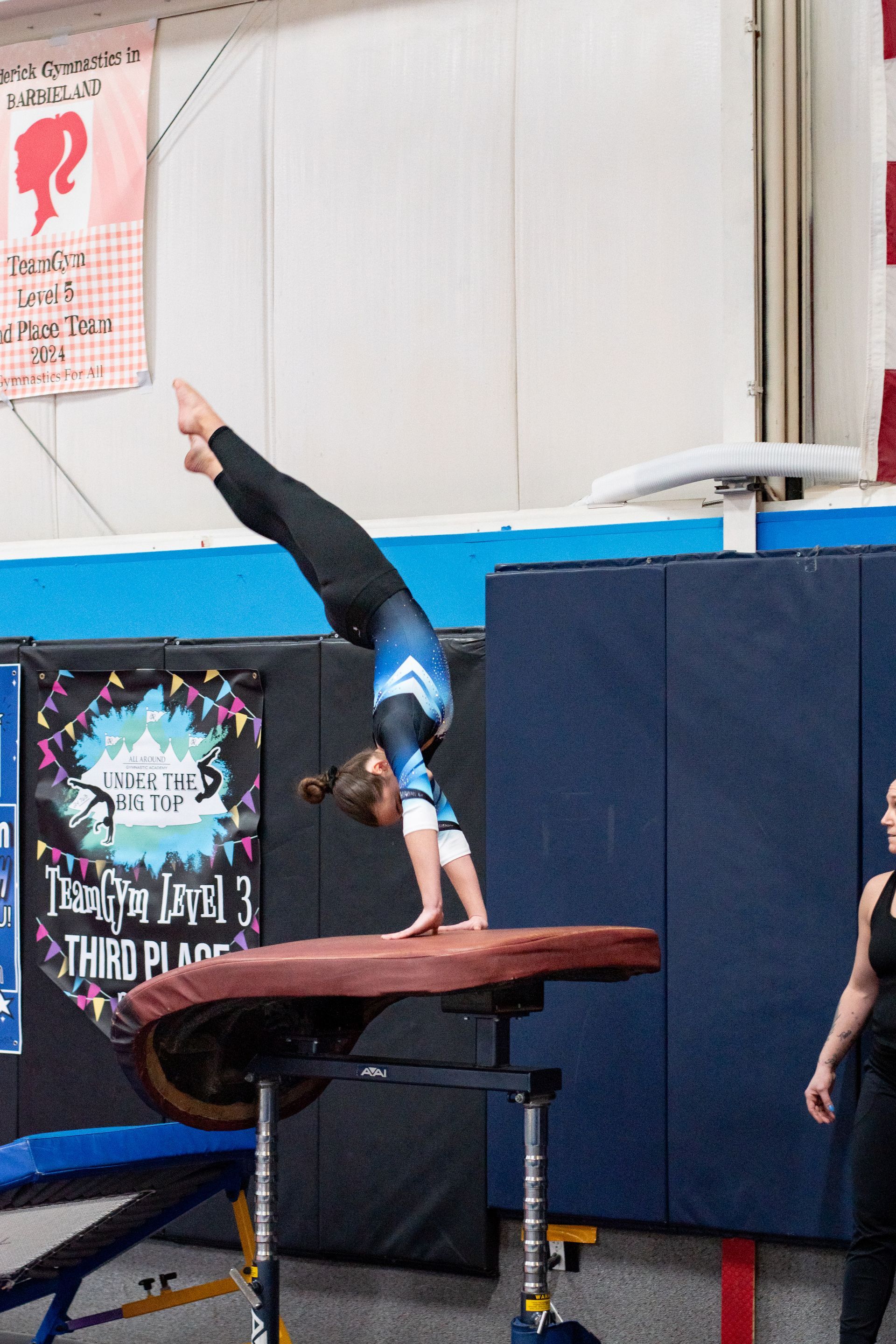Gymnast doing a handstand on a balance beam in an indoor gym.