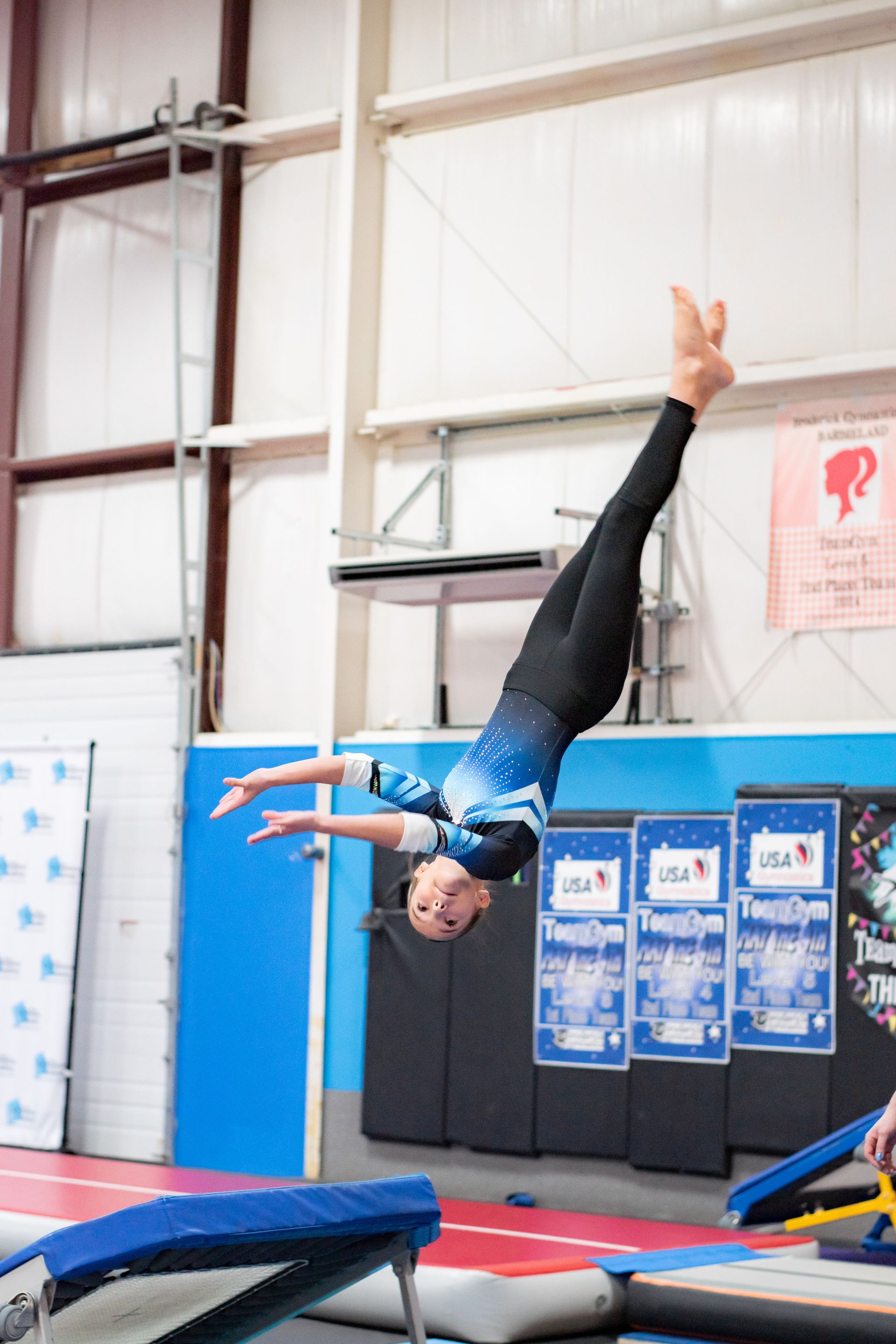 Gymnast inverted mid-air over a blue mat in an indoor training gym.