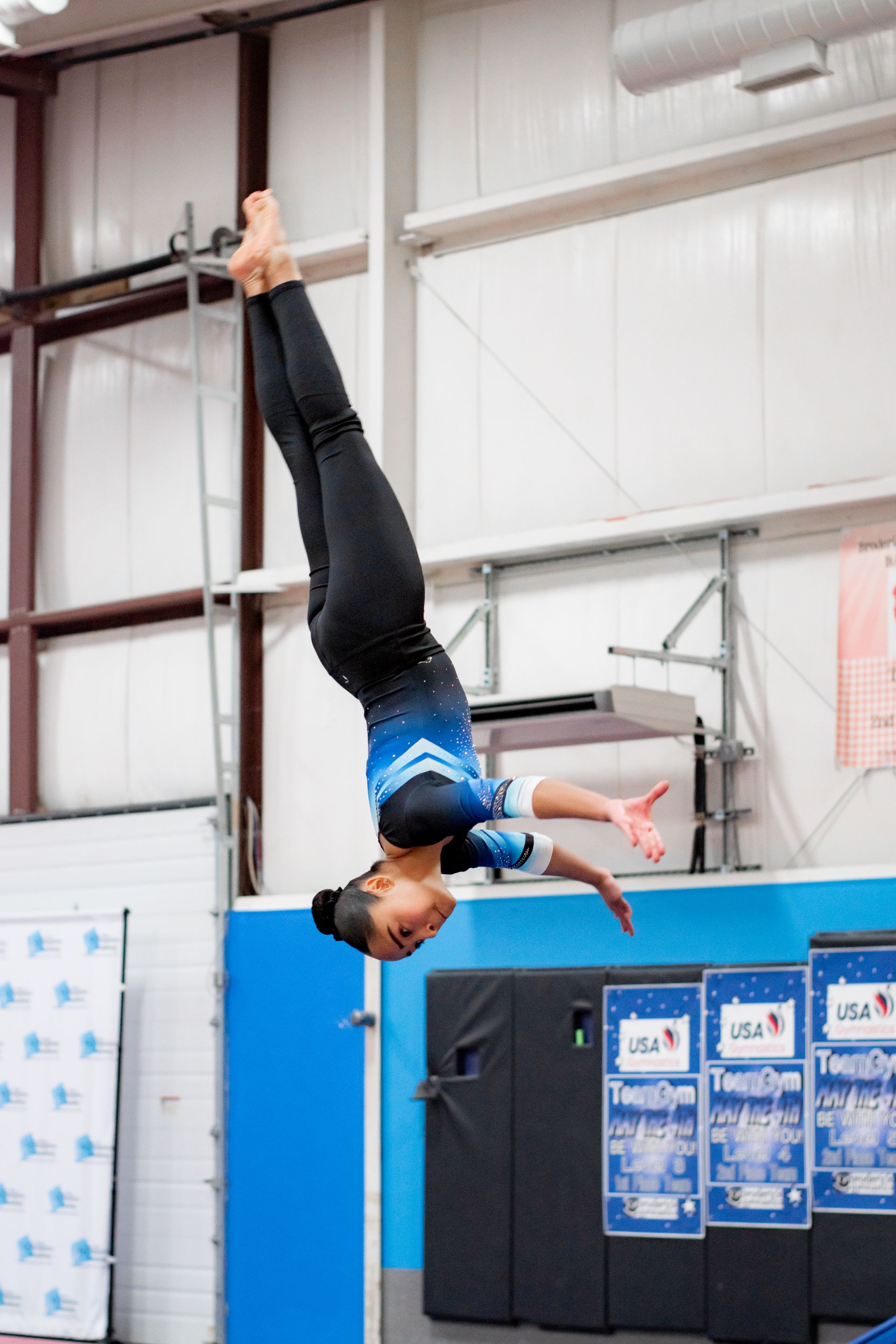 Gymnast upside down on a bar in a blue and white indoor training facility
