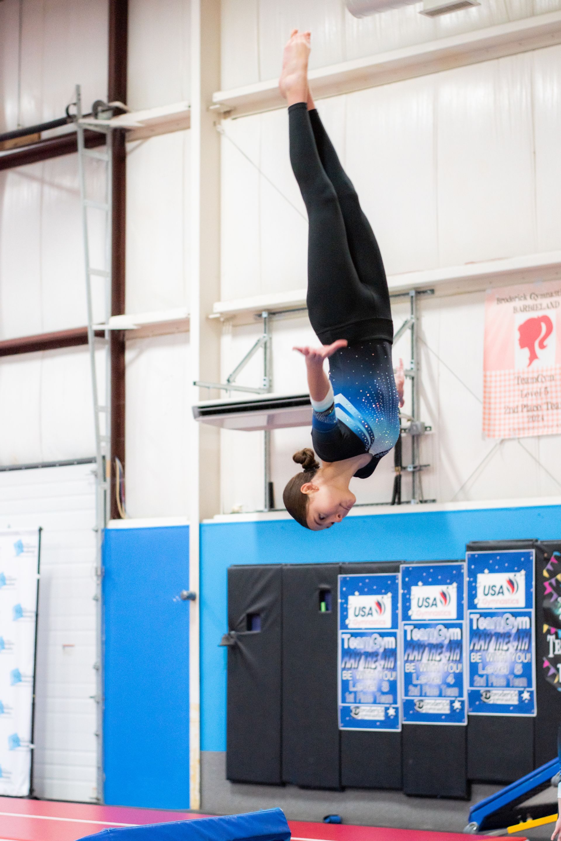 Gymnast performing a vertical handstand on a high bar in an indoor gymnasium