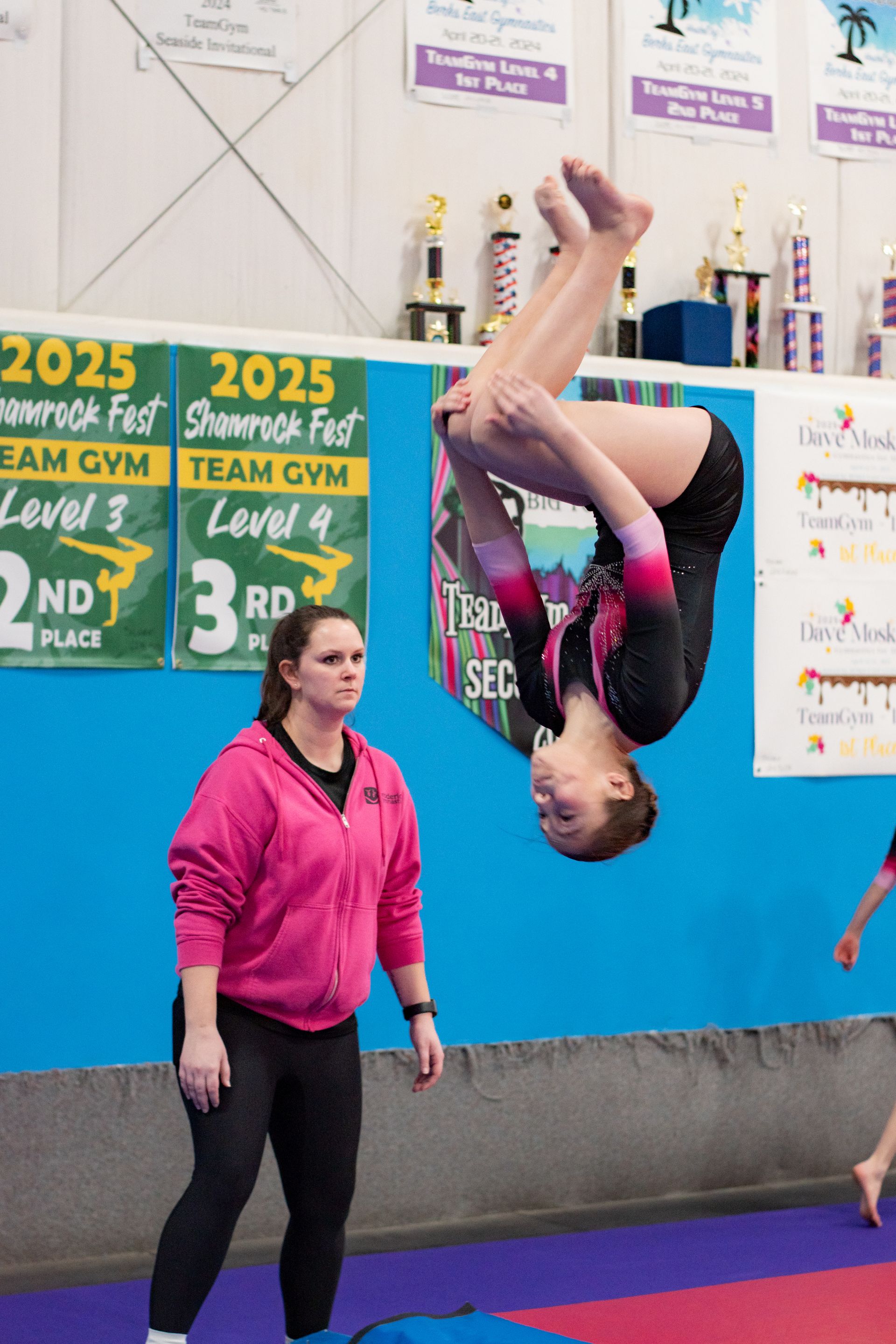 Gymnast upside down mid-flip beside a coach in a sports gym