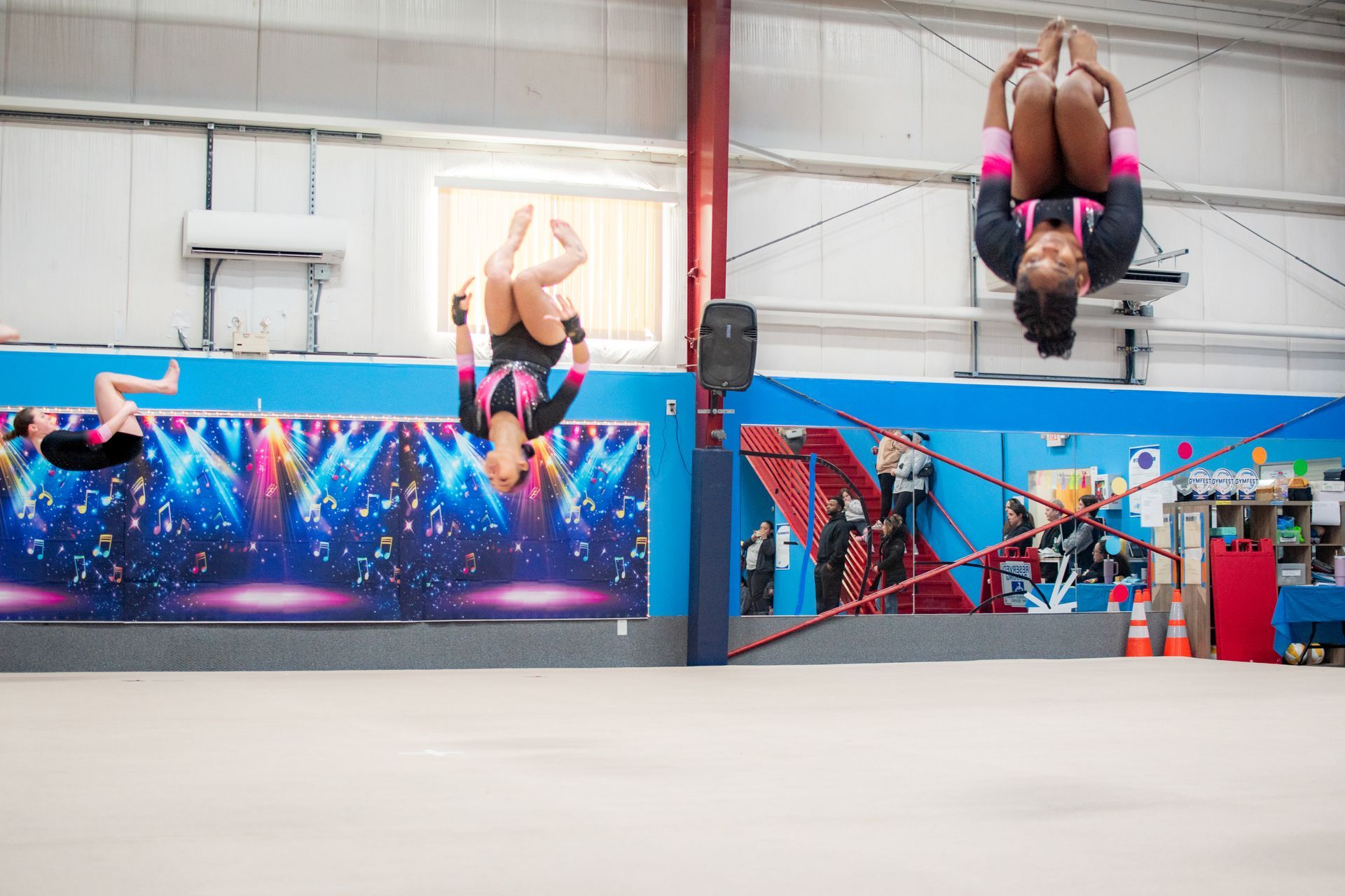 Two gymnasts flipping upside down in a bright training gym with colorful murals