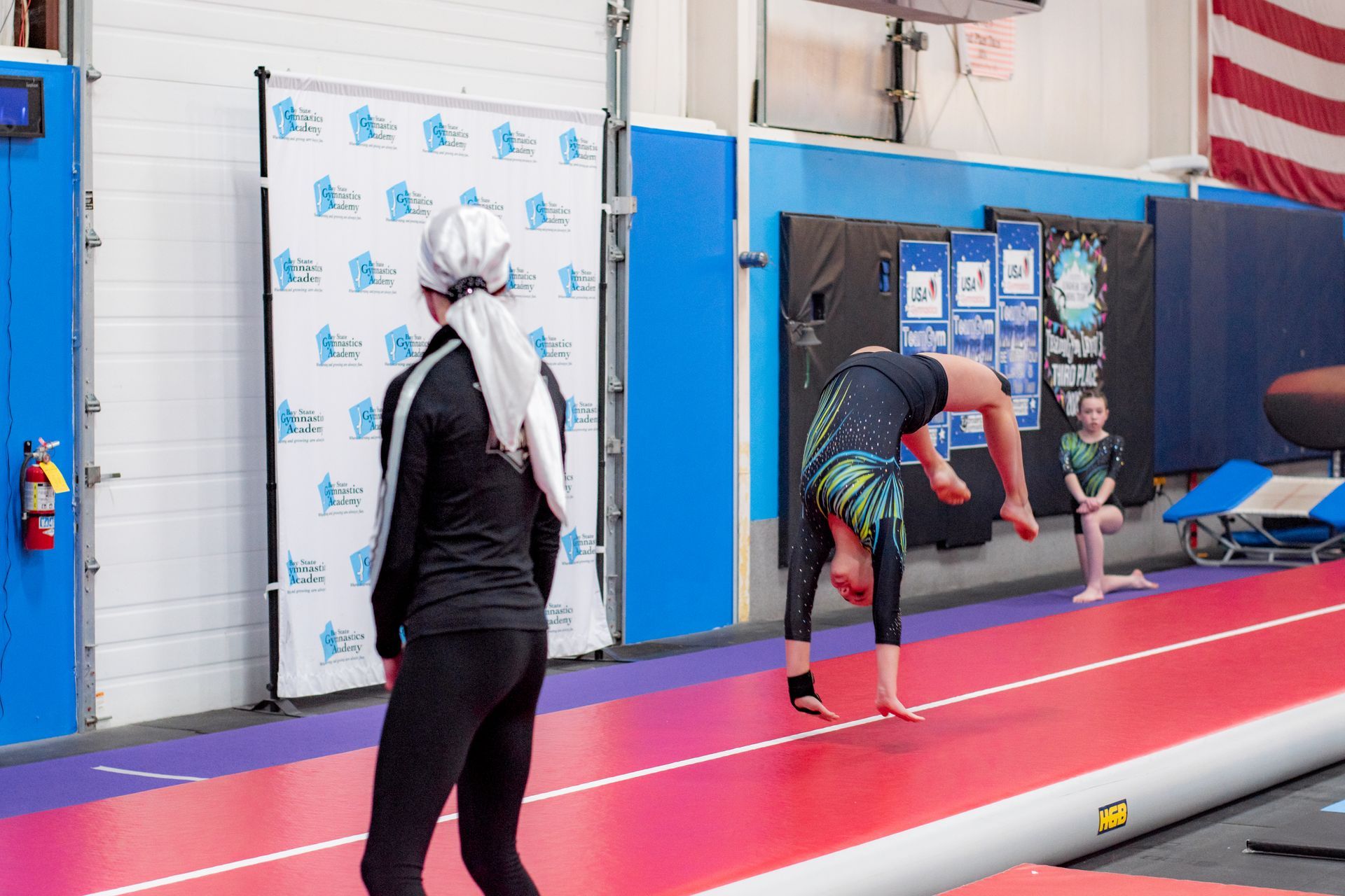 Athletes doing gymnastic floor exercises on a red mat in an indoor training hall