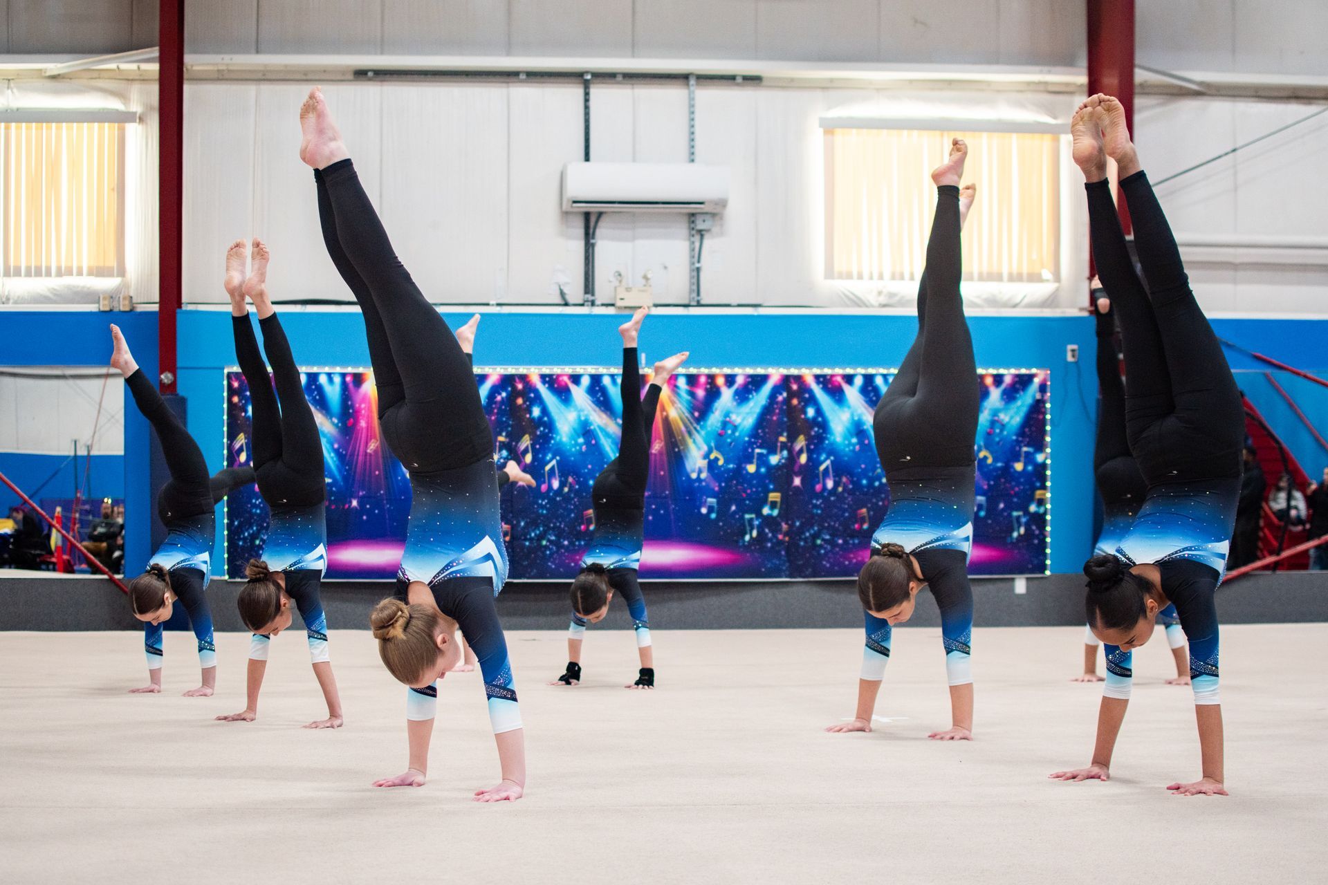 Gymnasts doing handstands in a gym, with blue wall padding and windows in the background
