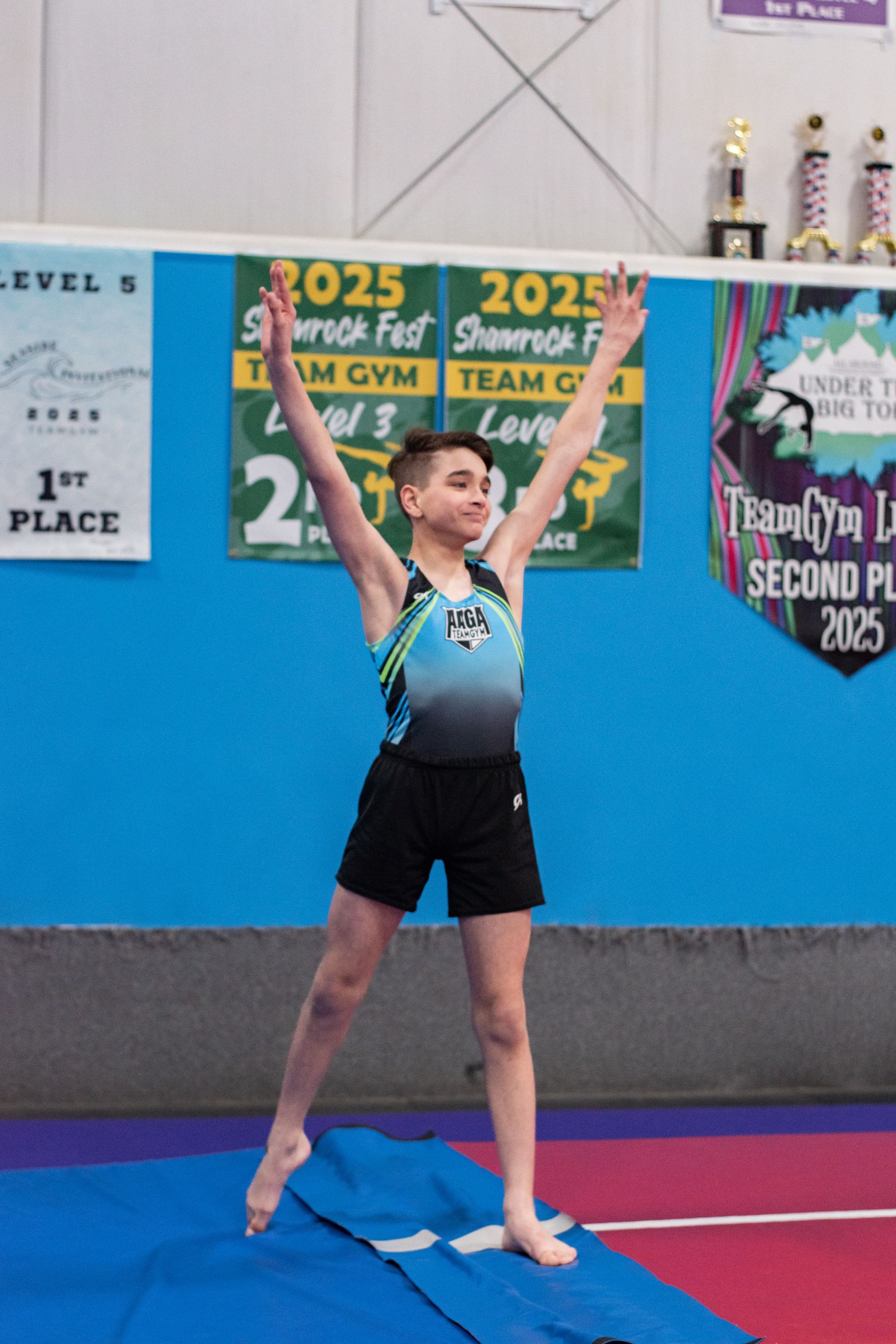 Gymnast posing with arms raised on a mat in a colorful gym