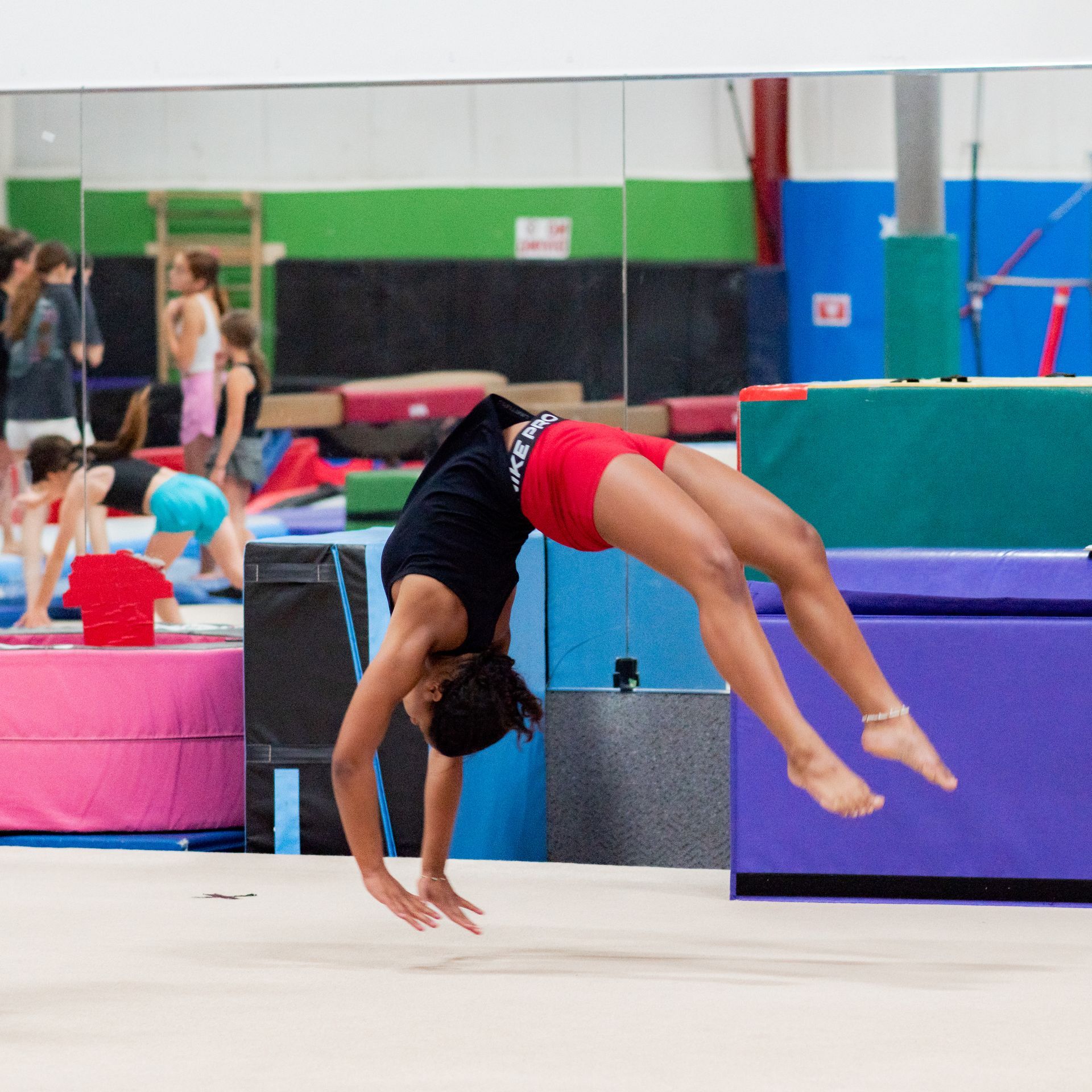 Gymnast mid-backbend on a mat in a colorful indoor gym