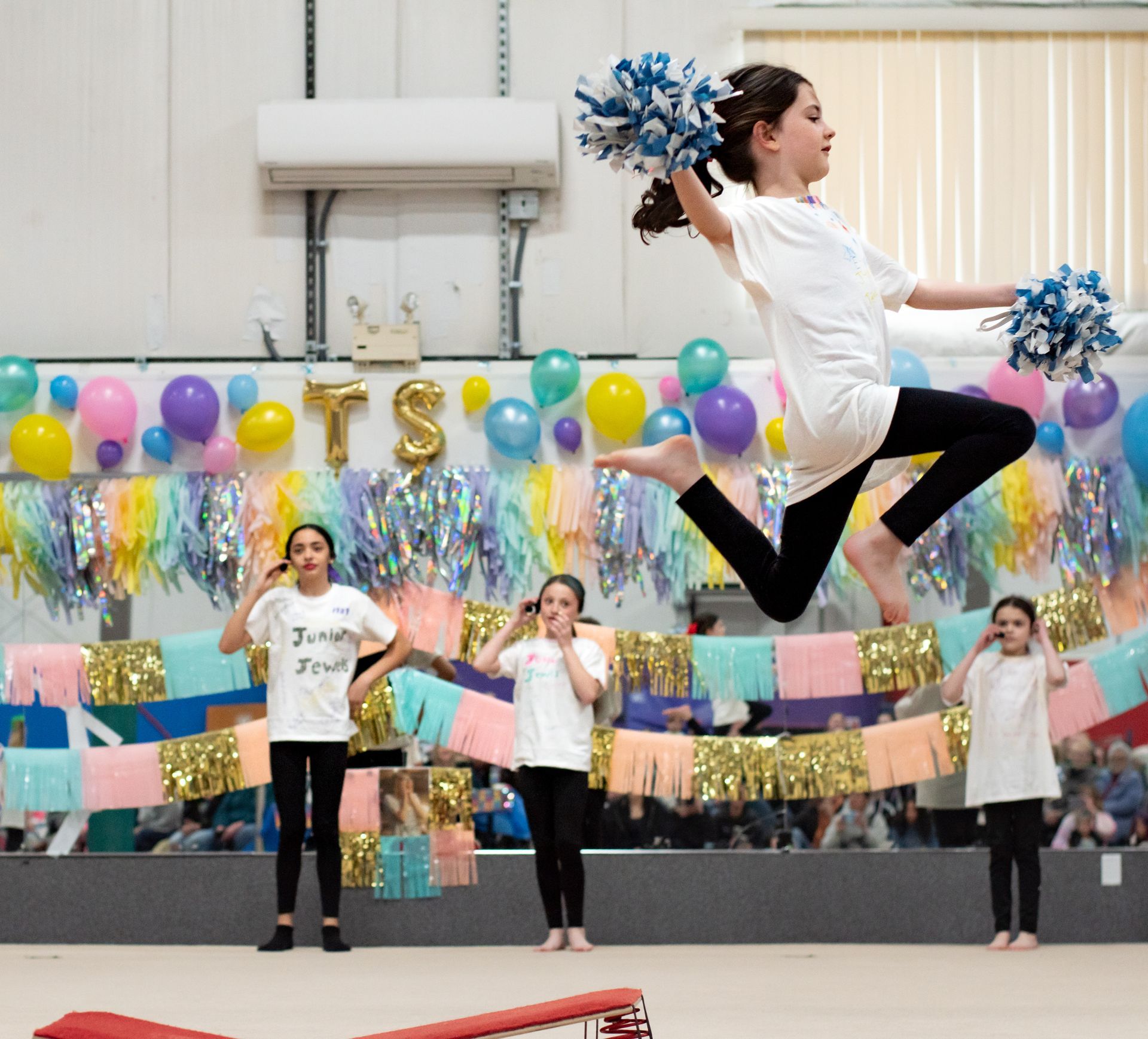Cheerleaders performing a stunt in a gym, with two flyers raised high and spectators watching.