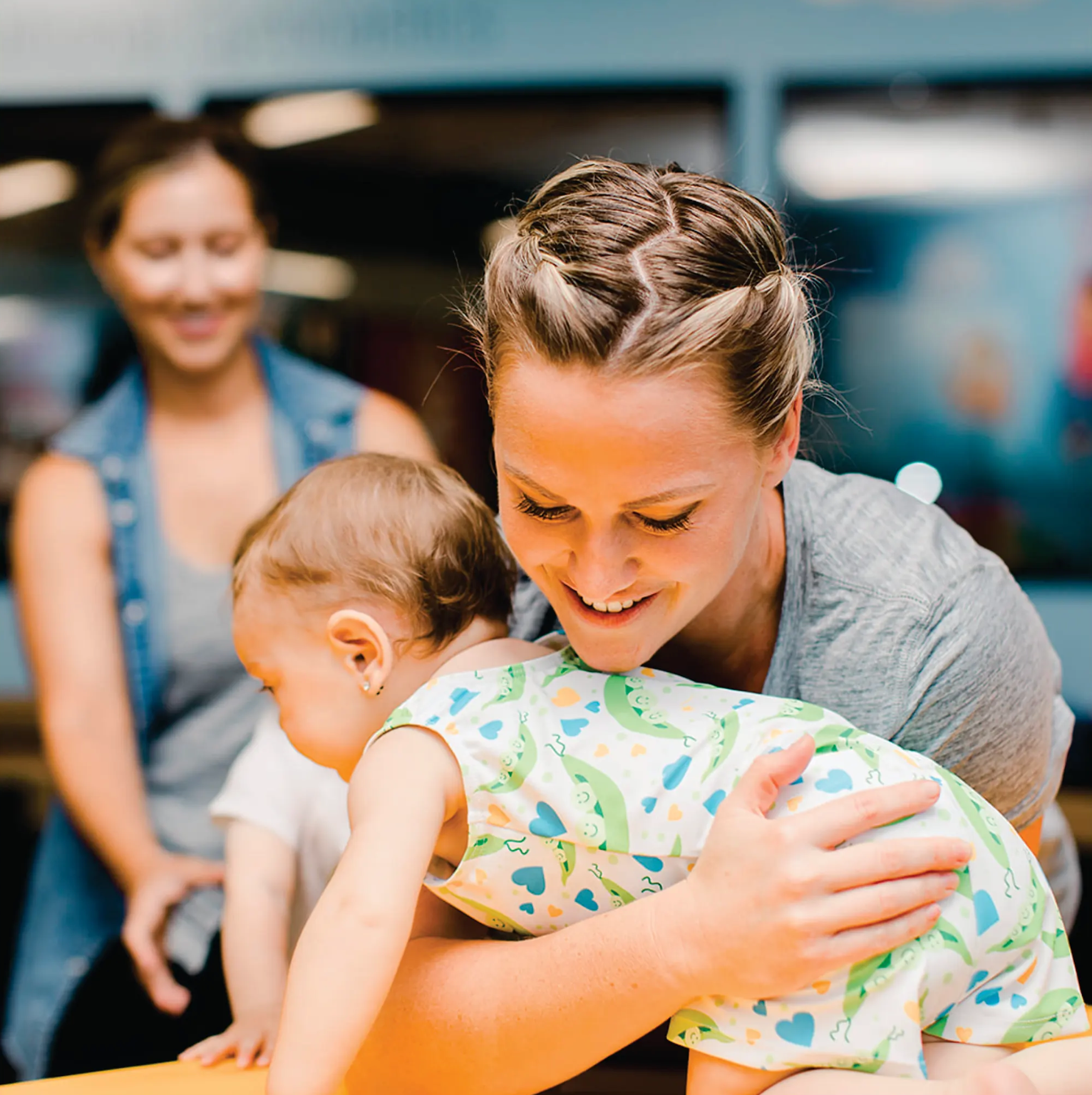 Woman hugging a child indoors, with another woman smiling in the background