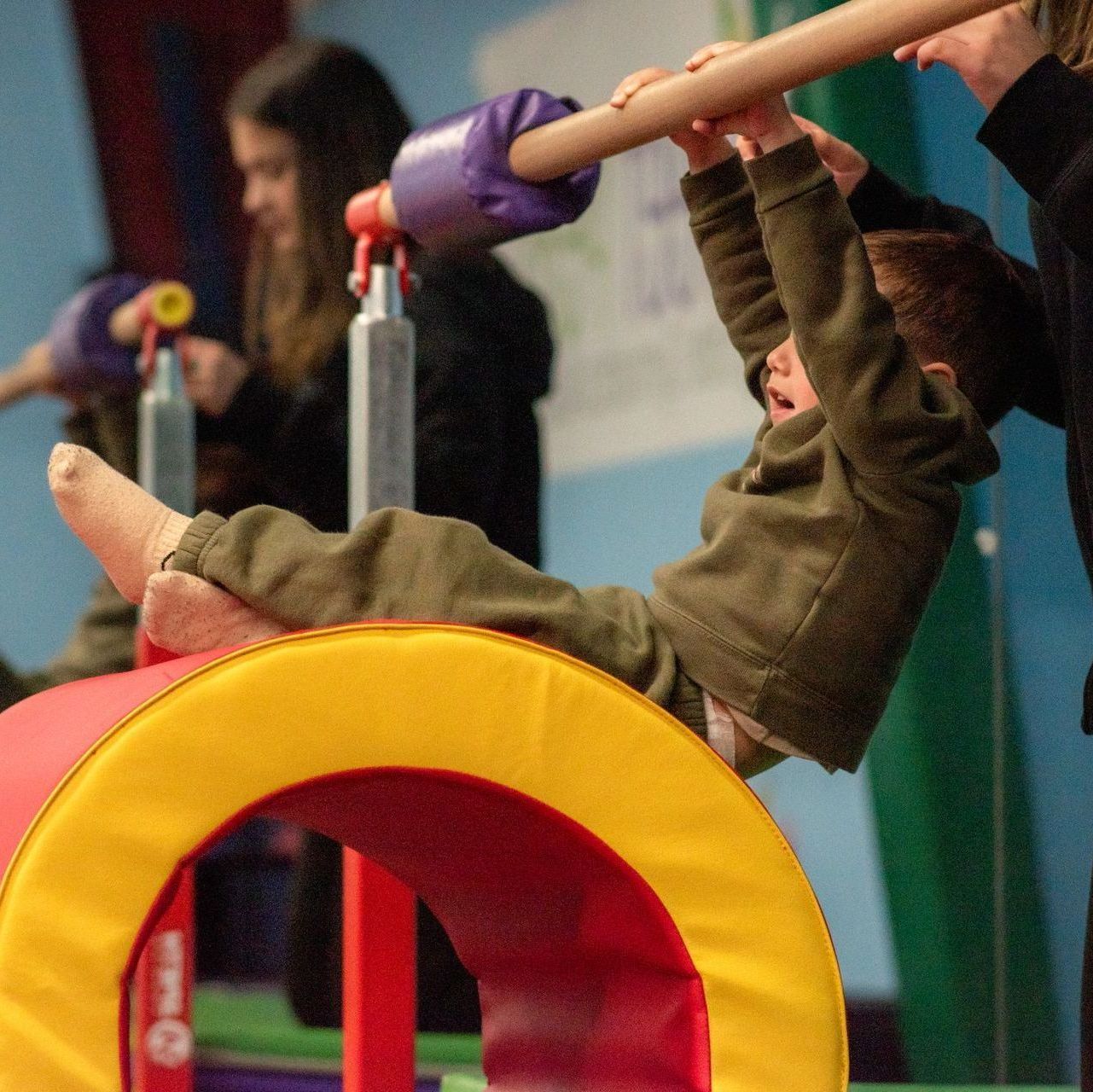 Child on indoor playground equipment, hanging upside down from a wooden bar with colorful rings in front
