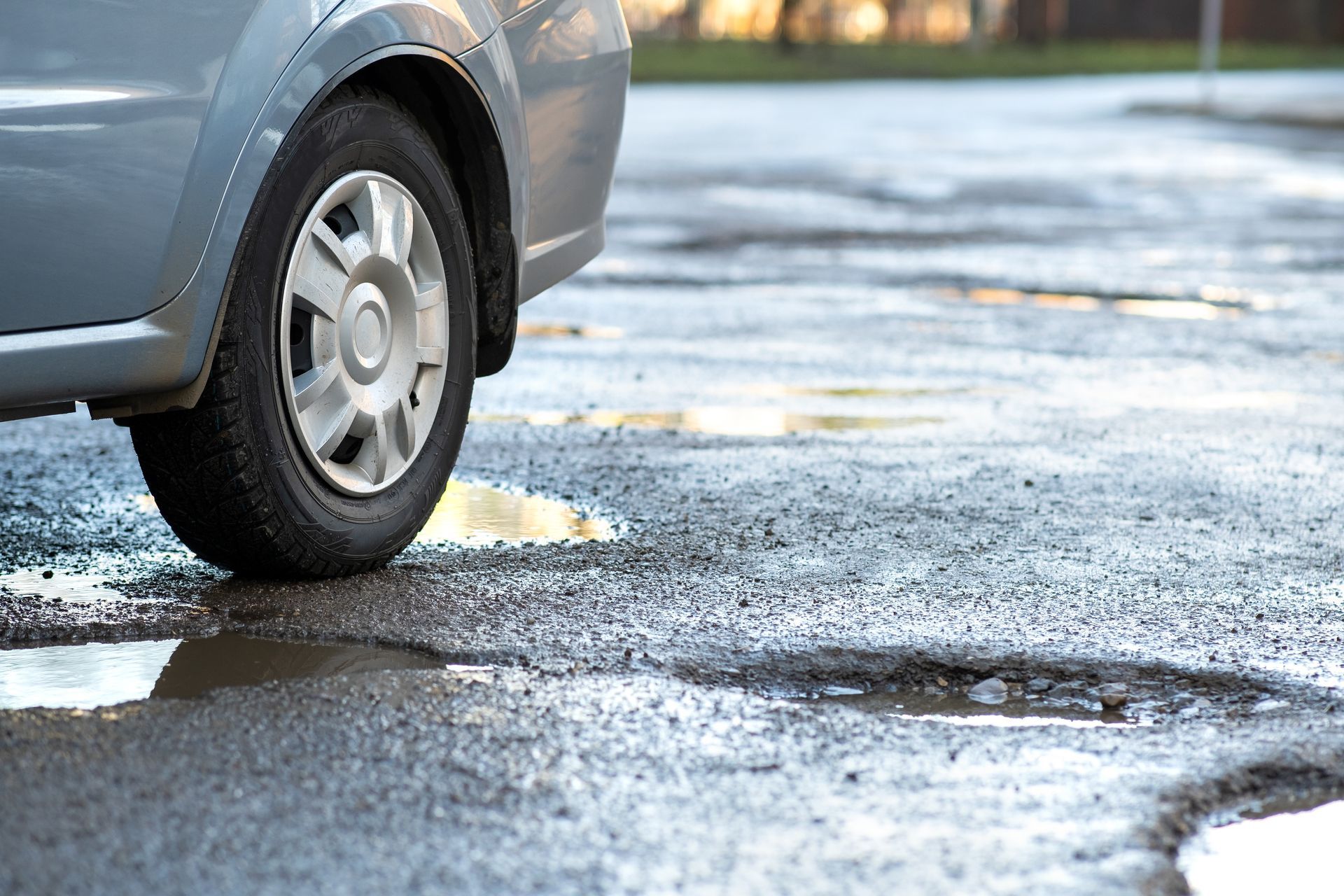 Car tire near a deep pothole filled with water on a damaged and uneven asphalt road. Car tire near a deep pothole filled with water on a damaged and uneven asphalt road.