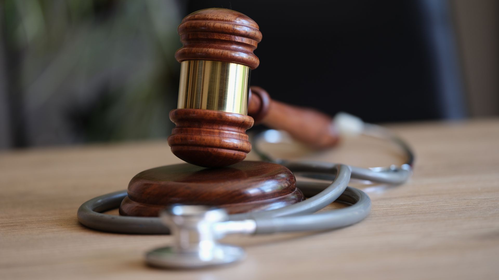 Wooden judge’s gavel resting on a stethoscope on a desk, symbolizing medical law and justice.