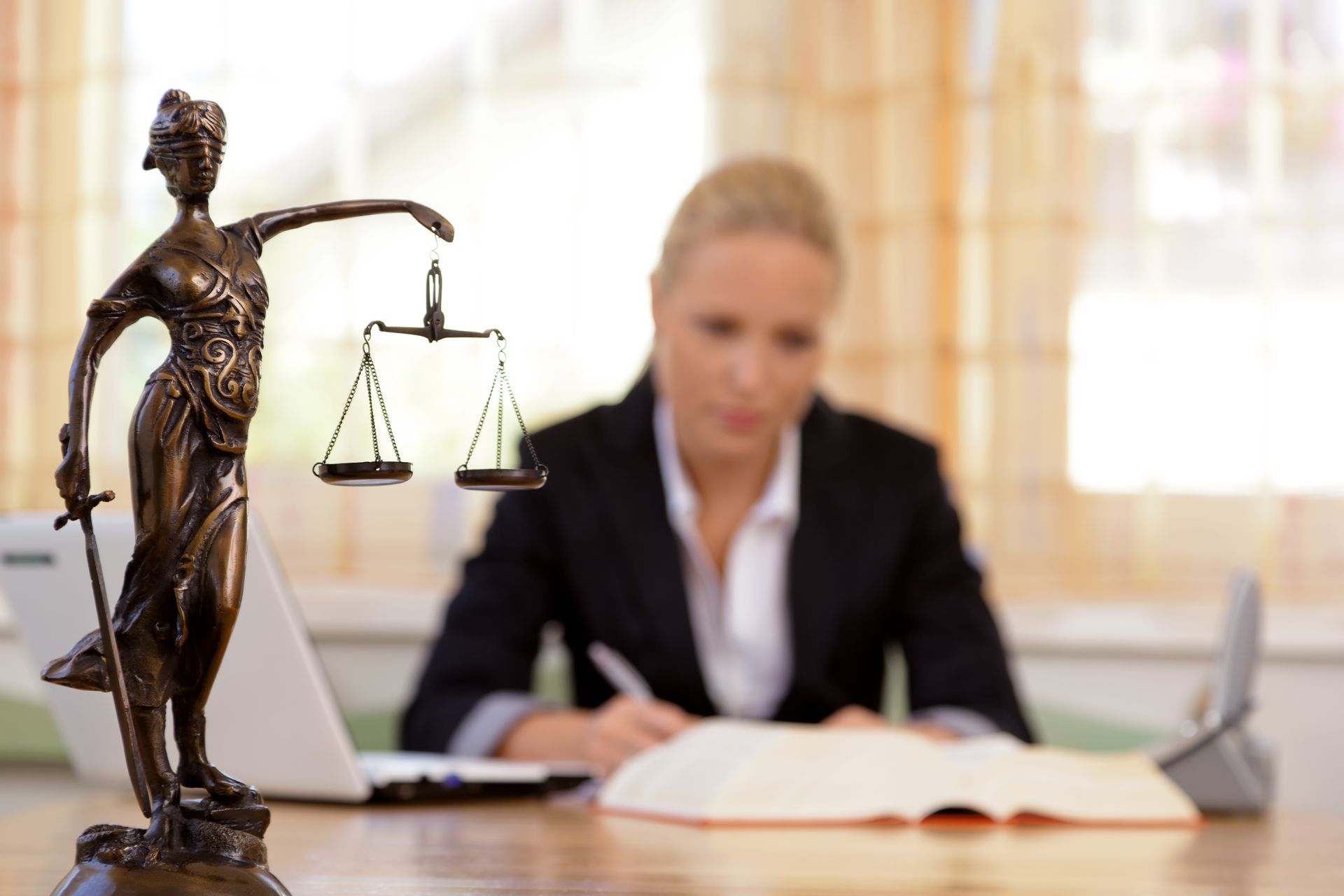 Statue of Lady Justice with scales; blurred background of a person in a suit writing at a desk.