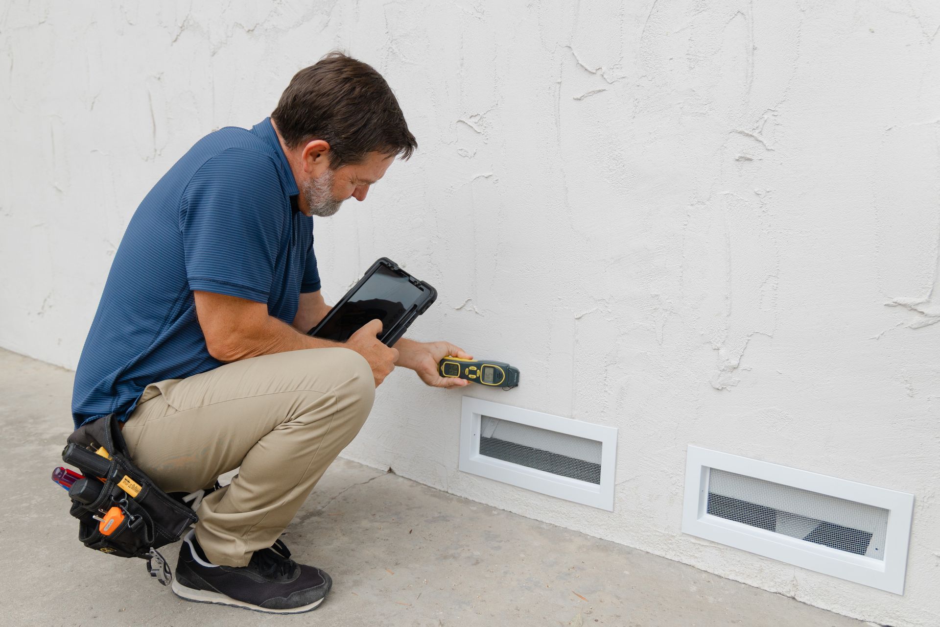Worker inspecting a wall vent with a handheld tool