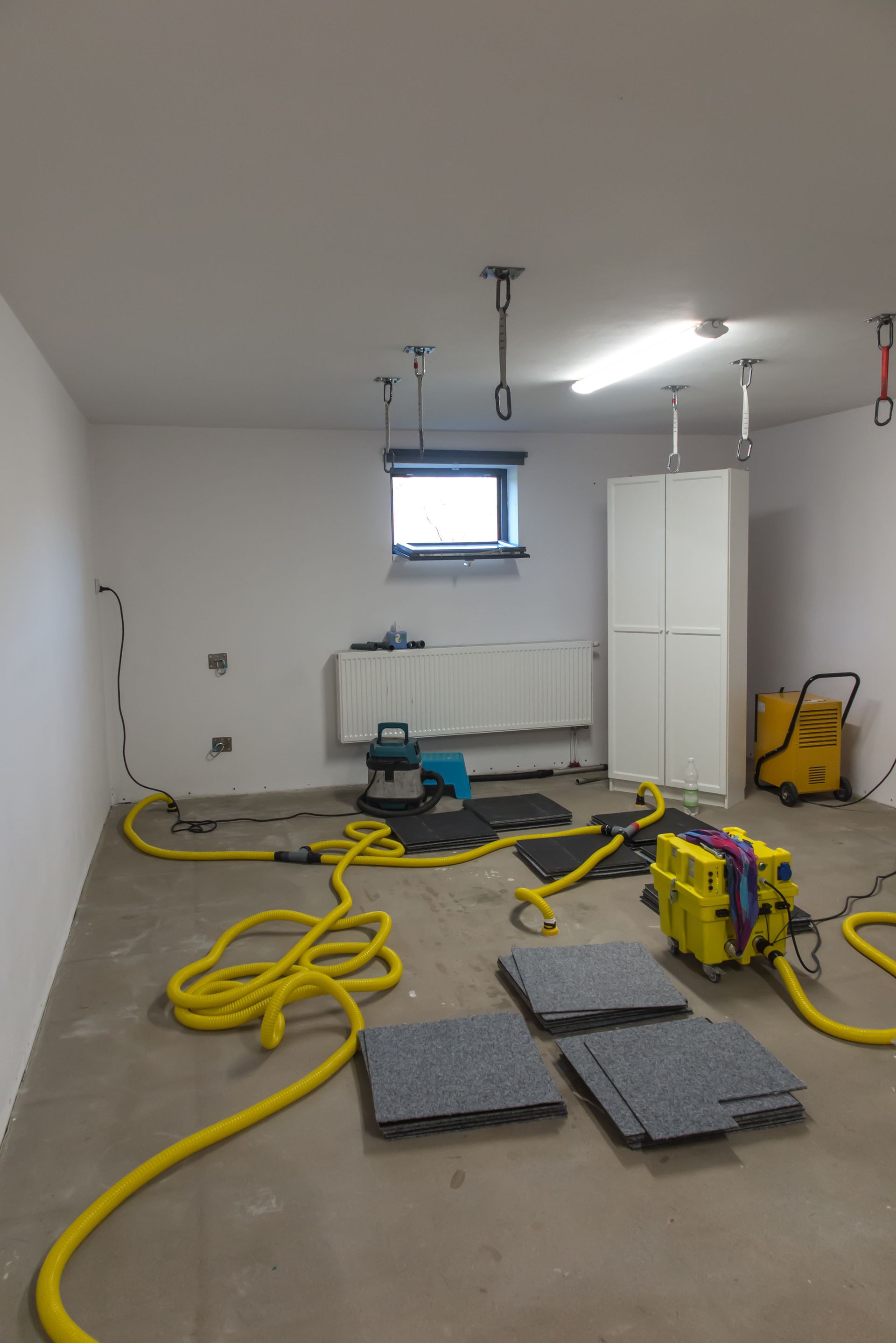 Renovation room with yellow power tools, coiled cables, floor mats, and exposed hanging lights