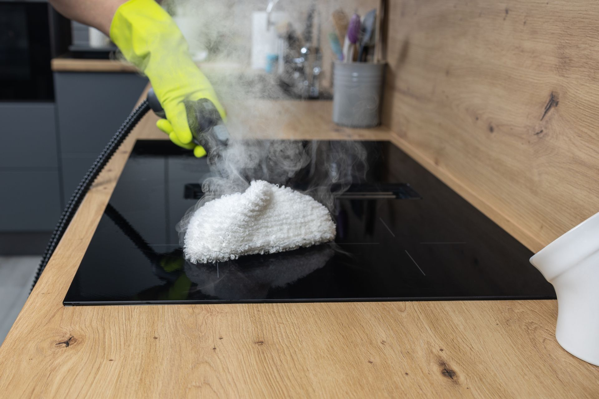 Gloved hand wiping a black glass stovetop with a white cloth in a kitchen