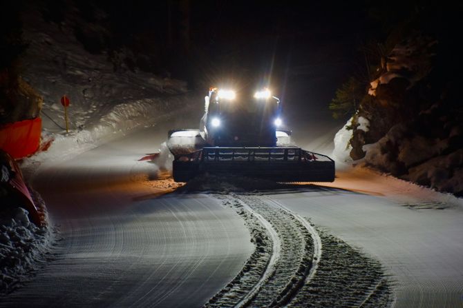 Snowplow clearing a snowy mountain road at night, headlights shining in the dark.
