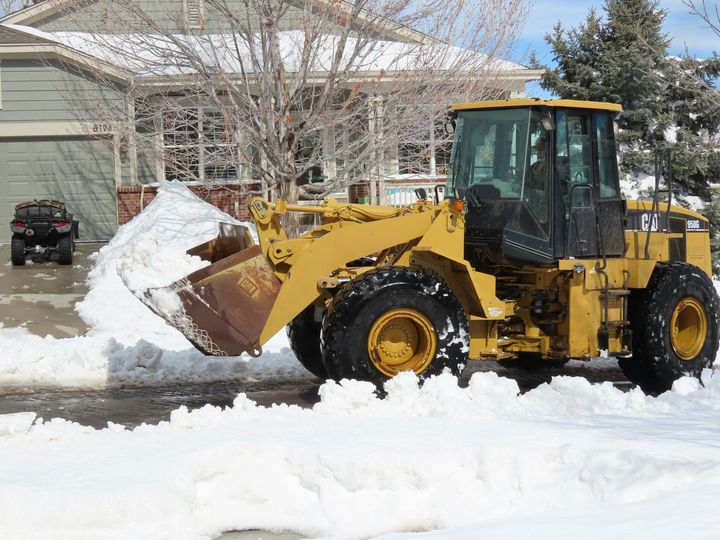 Yellow front loader clearing snow in a residential driveway