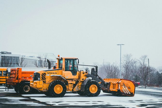 Orange snowplow truck clearing a snowy parking lot on an overcast winter day