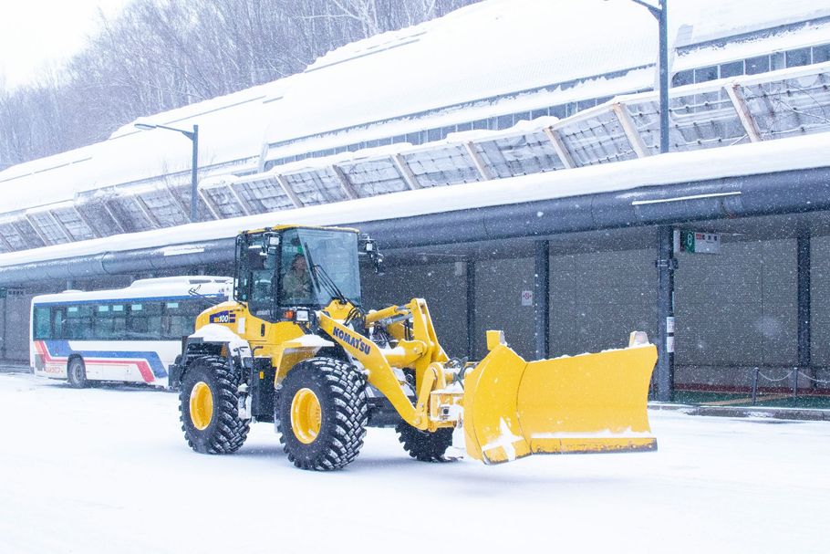 Yellow snowplow clearing snow at a bus station in heavy snowfall