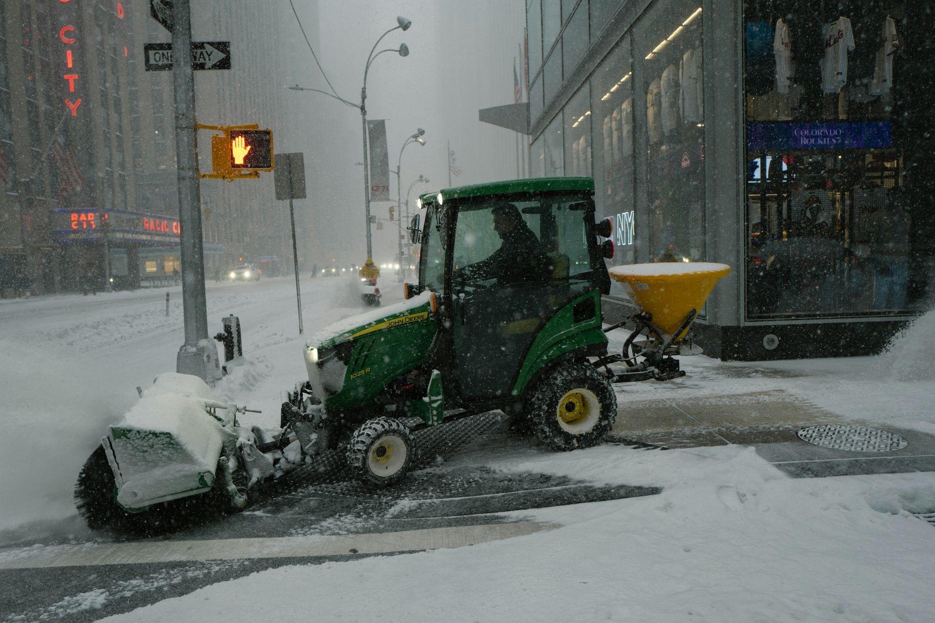Green snowplow clearing a snowy city street during a heavy snowfall