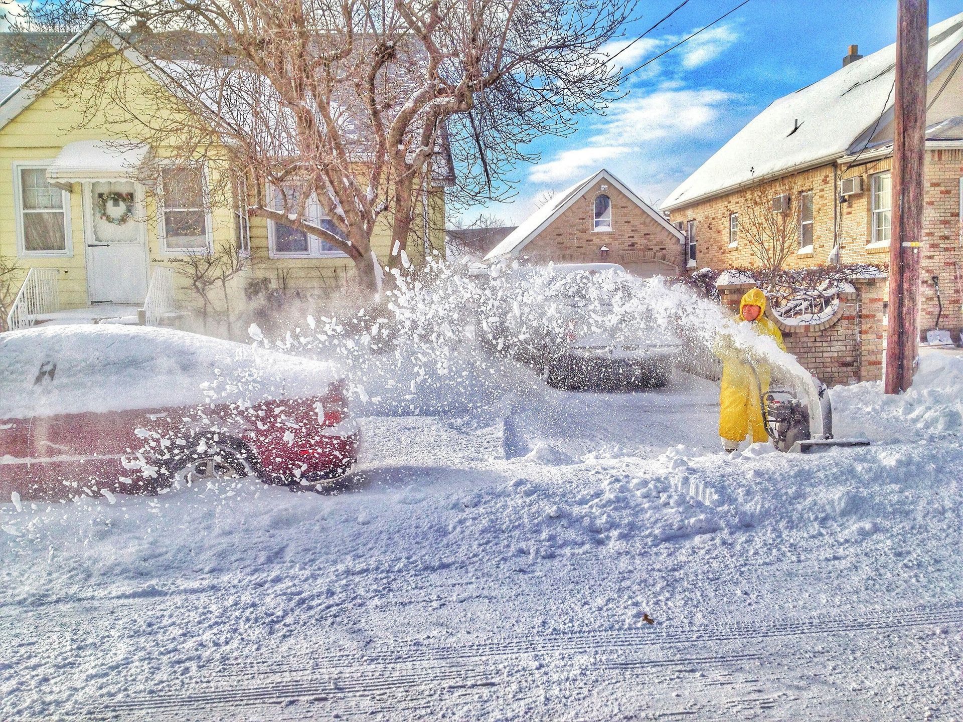Snow-covered street with a person snowblowing near houses after a heavy snowfall