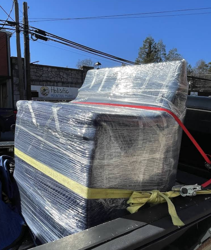 A wrapped and secured piece of furniture in a truck bed, held by straps.