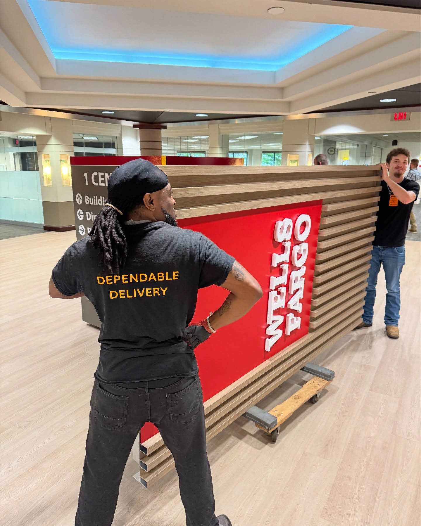 Two people moving a Wells Fargo sign inside a building.