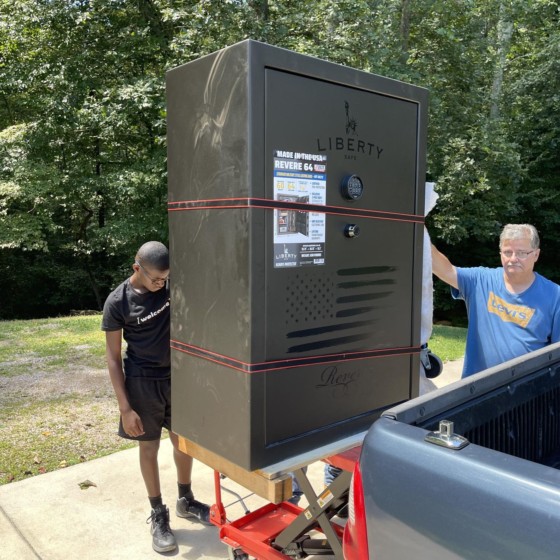 Two men loading a large black safe from a truck.